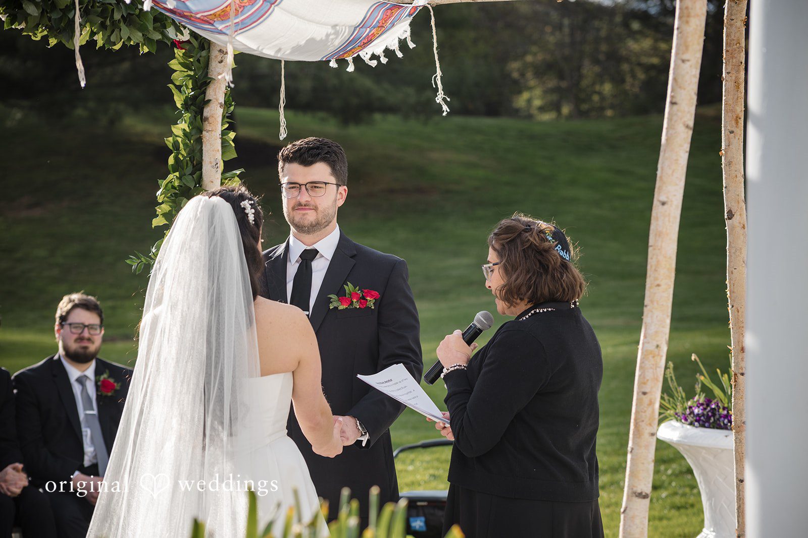 Bride smiles warmly at groom while holding hands during ceremony.