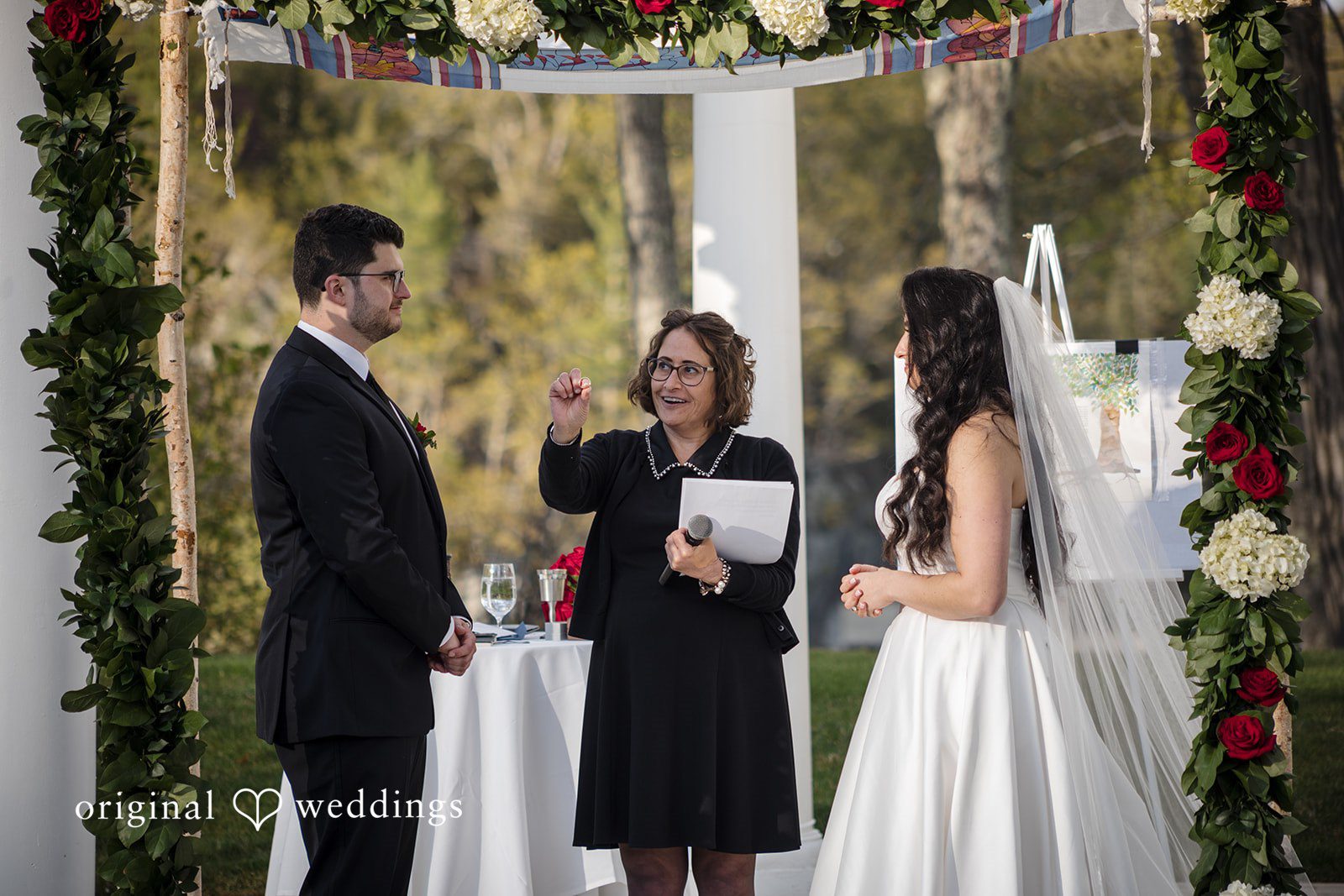 Ceremony moment as officiant speaks to couple beneath floral arch.