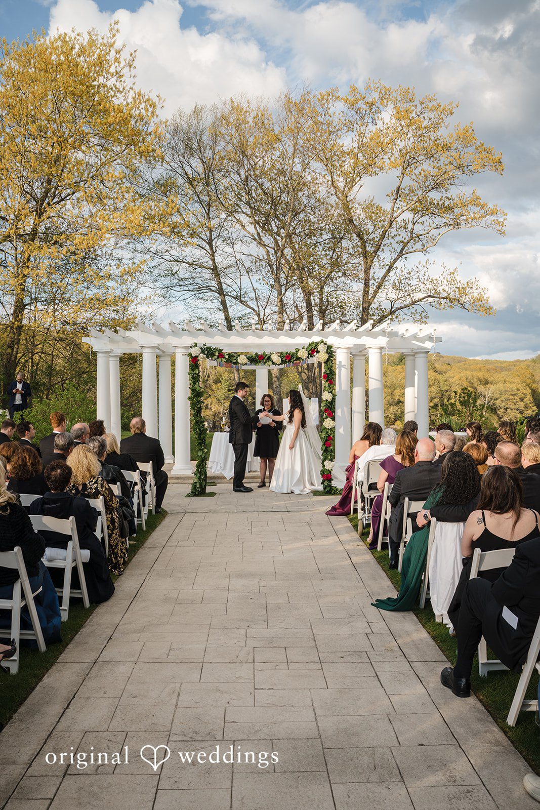 Elegant ceremony setup with floral arch and guests watching couple.