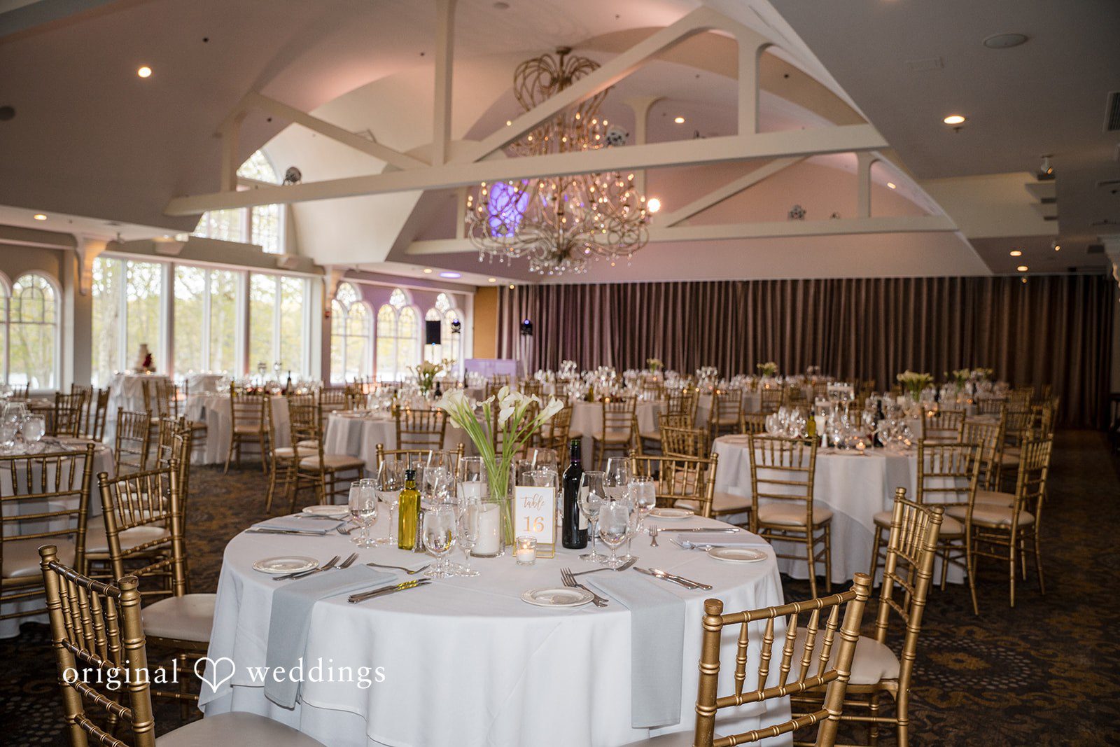 Romantic ballroom reception décor with chandelier lighting and gold chairs