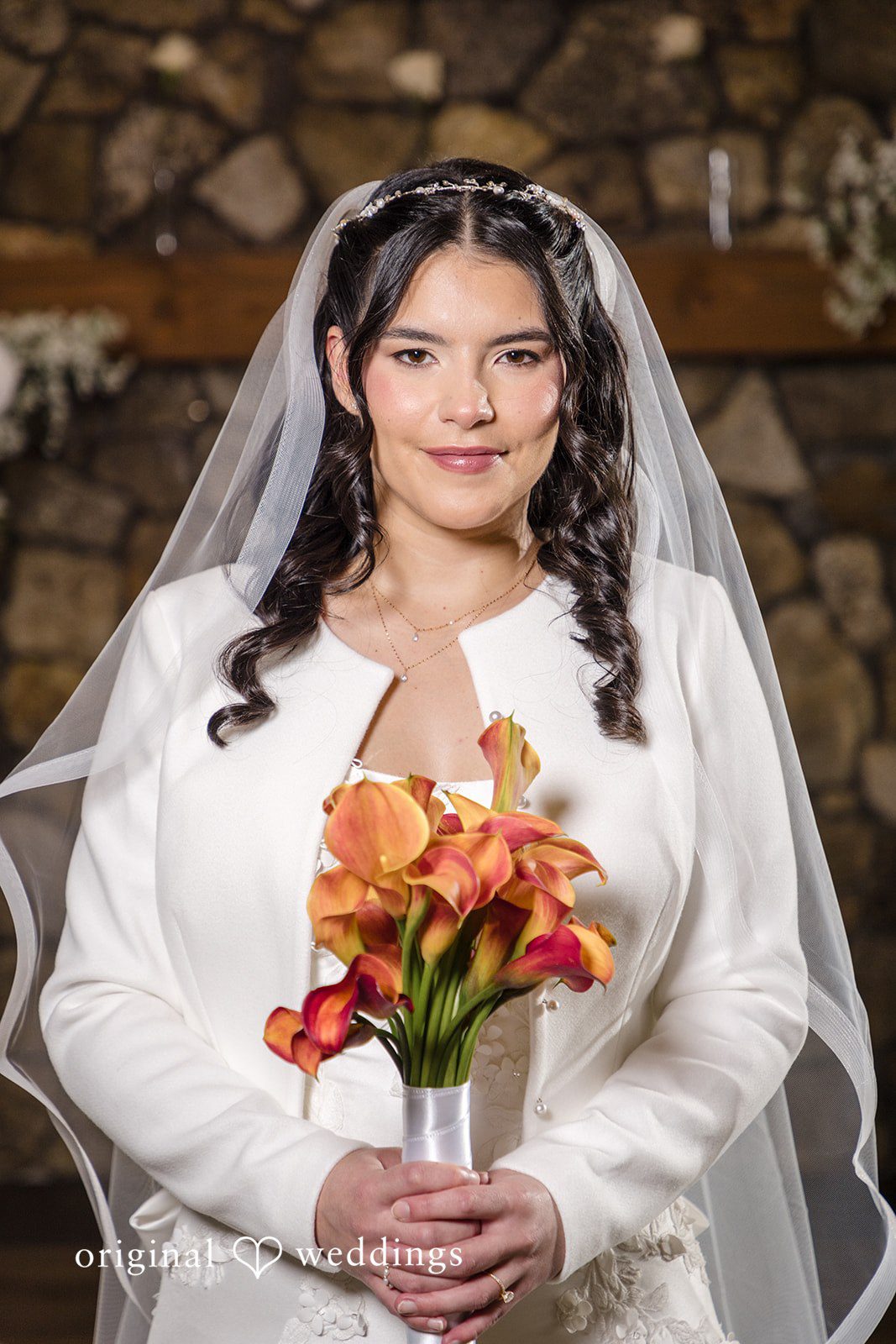 Maria + Eddy A smiling bride in a long-sleeved white gown holds an orange floral bouquet.