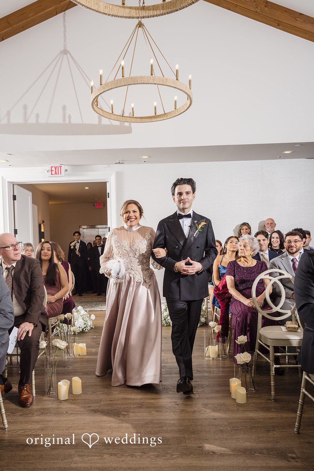 Maria + Eddy A groom and woman walk down the wedding aisle together while guests watch.