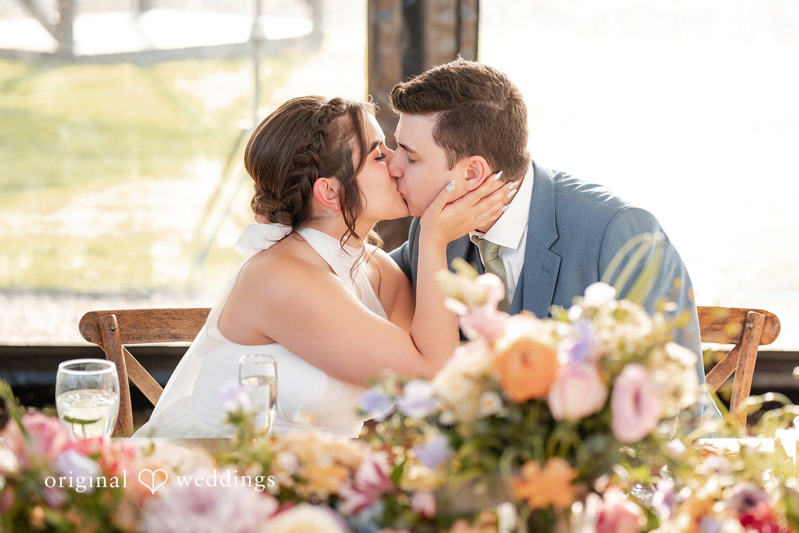 Bride and groom sharing a kiss at their wedding reception table.