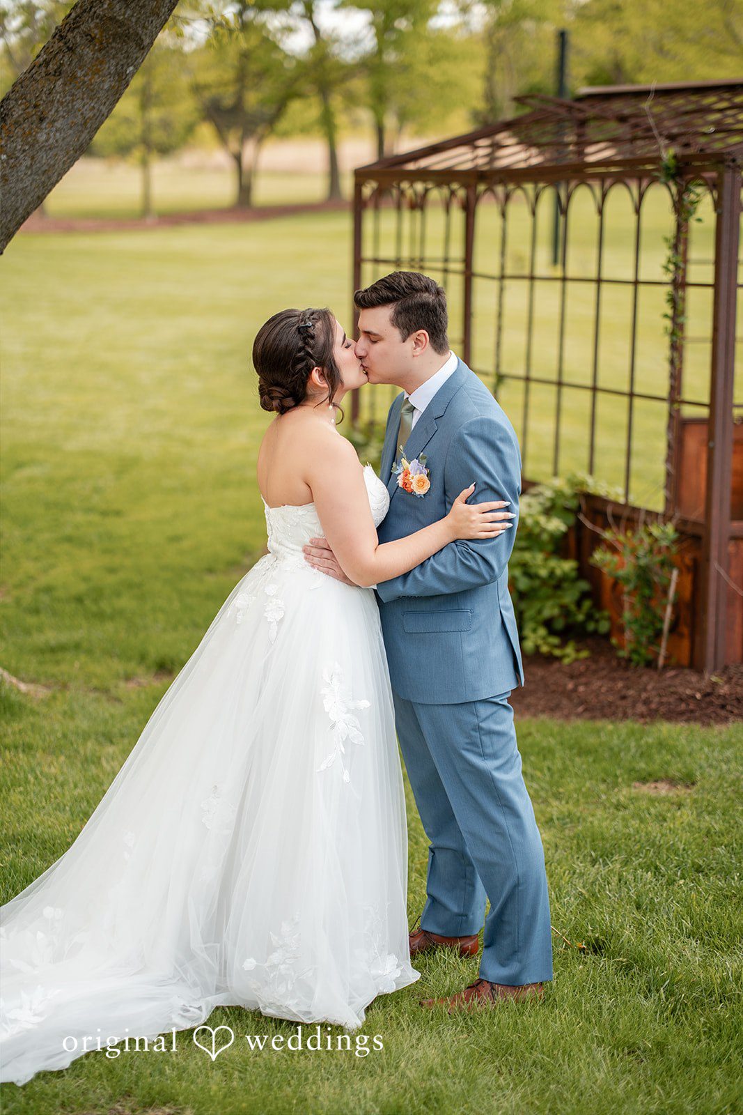 Bride and groom sharing a kiss on the lawn after their wedding ceremony.