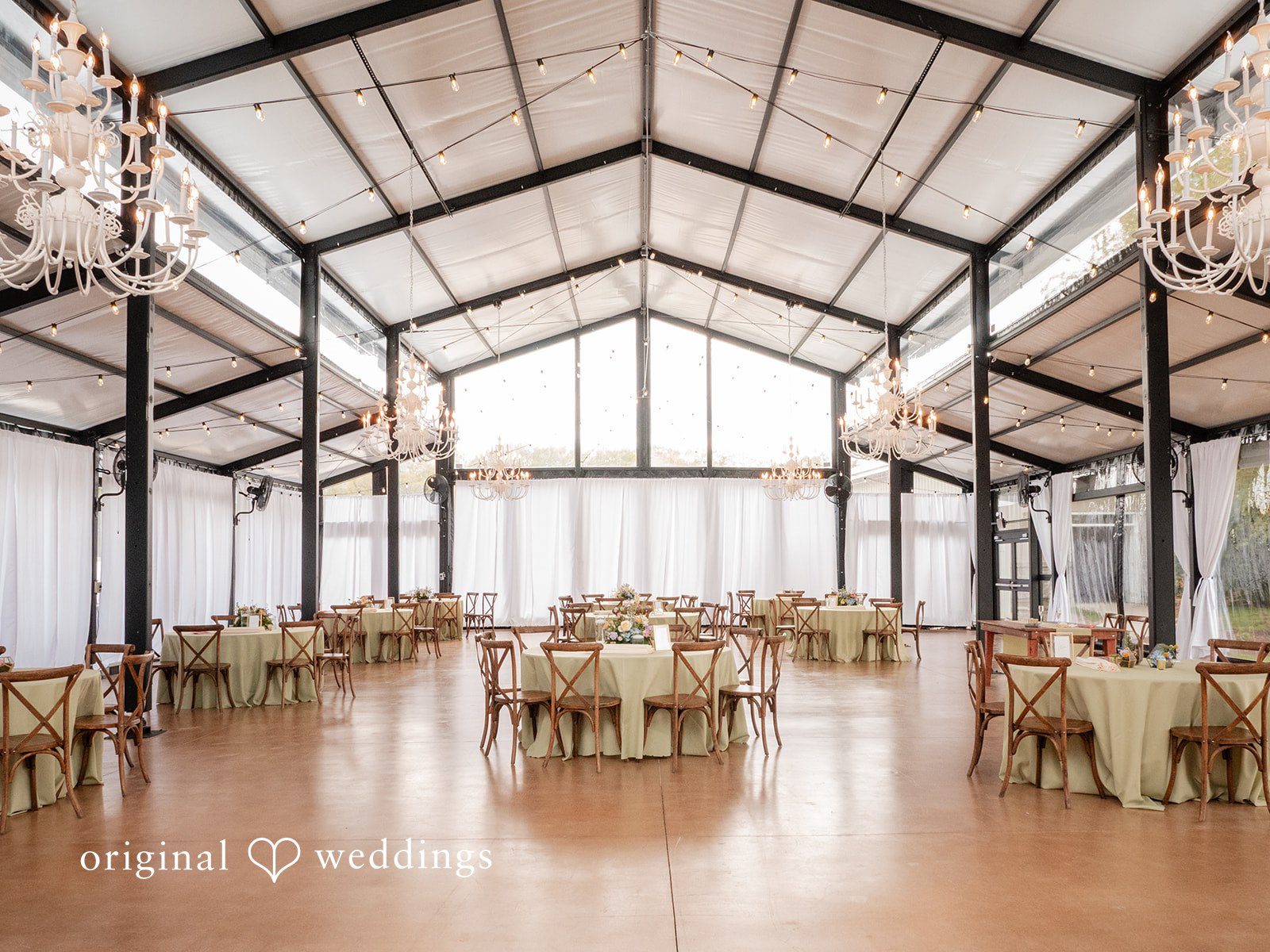 Wedding reception space with round tables, chandeliers, and elegant drapery.