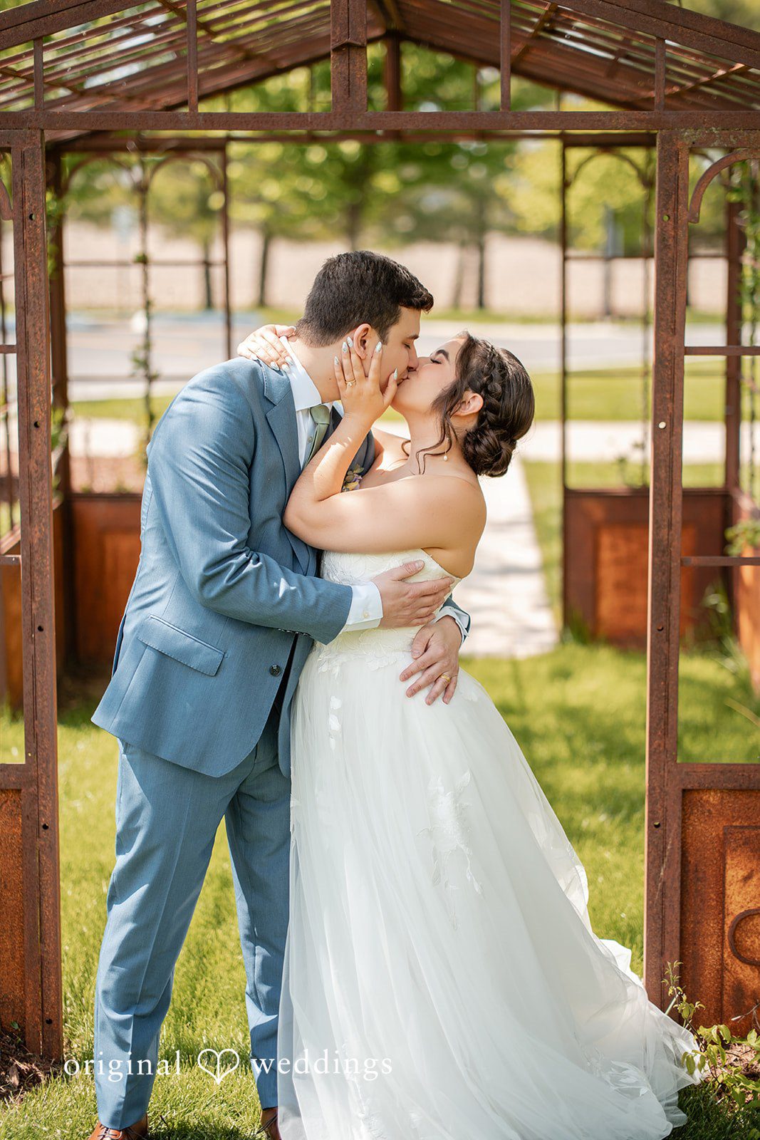 Bride and groom sharing a kiss beneath a rustic garden arbor.
