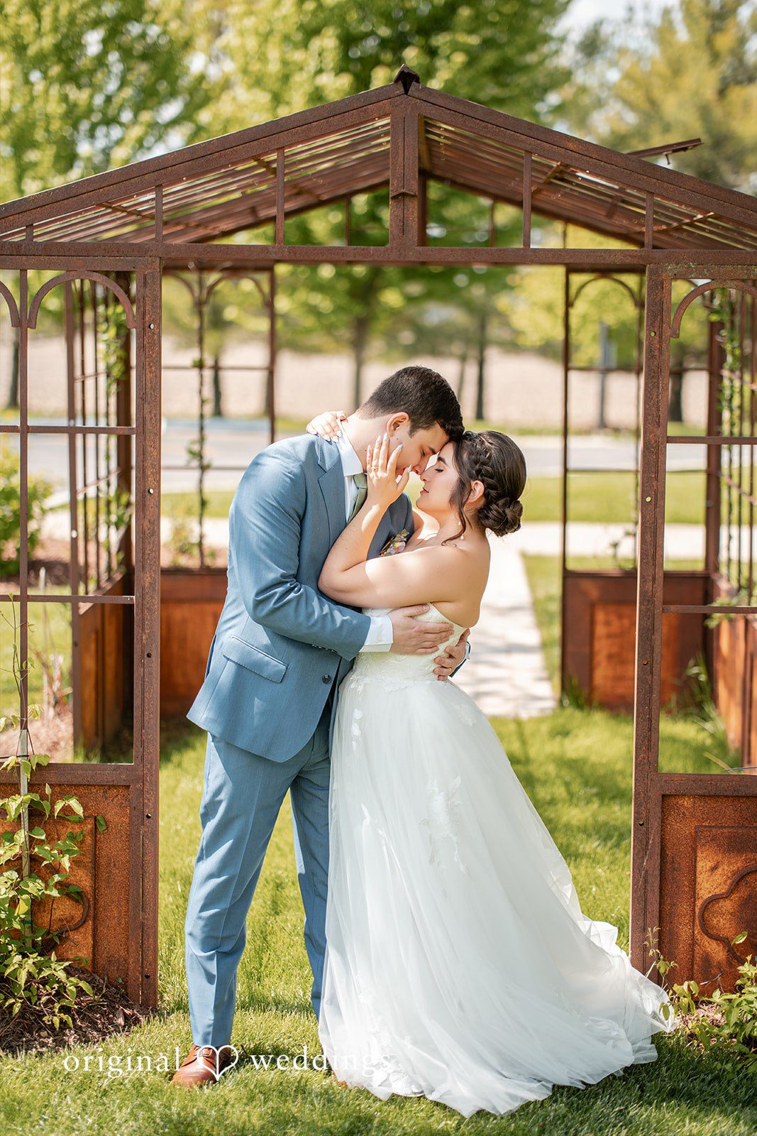 Bride and groom sharing a romantic kiss beneath a rustic garden arbor.