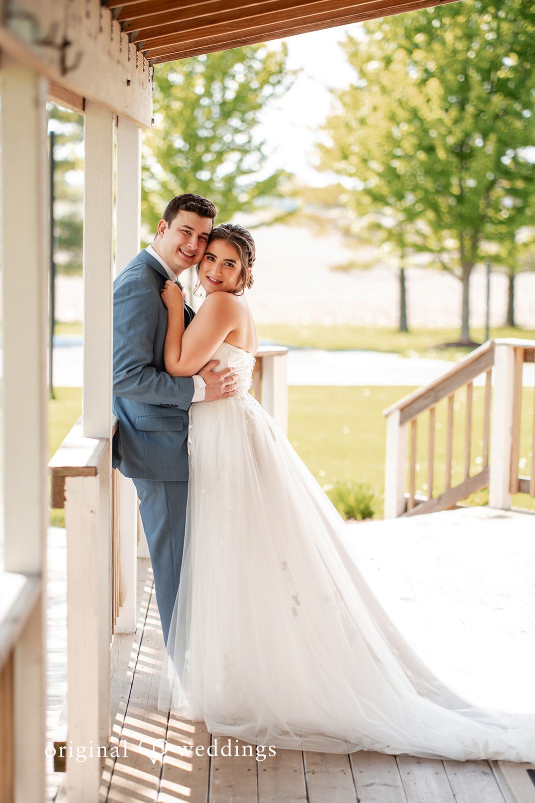 Bride and groom embracing on a sunlit porch during their wedding portraits.