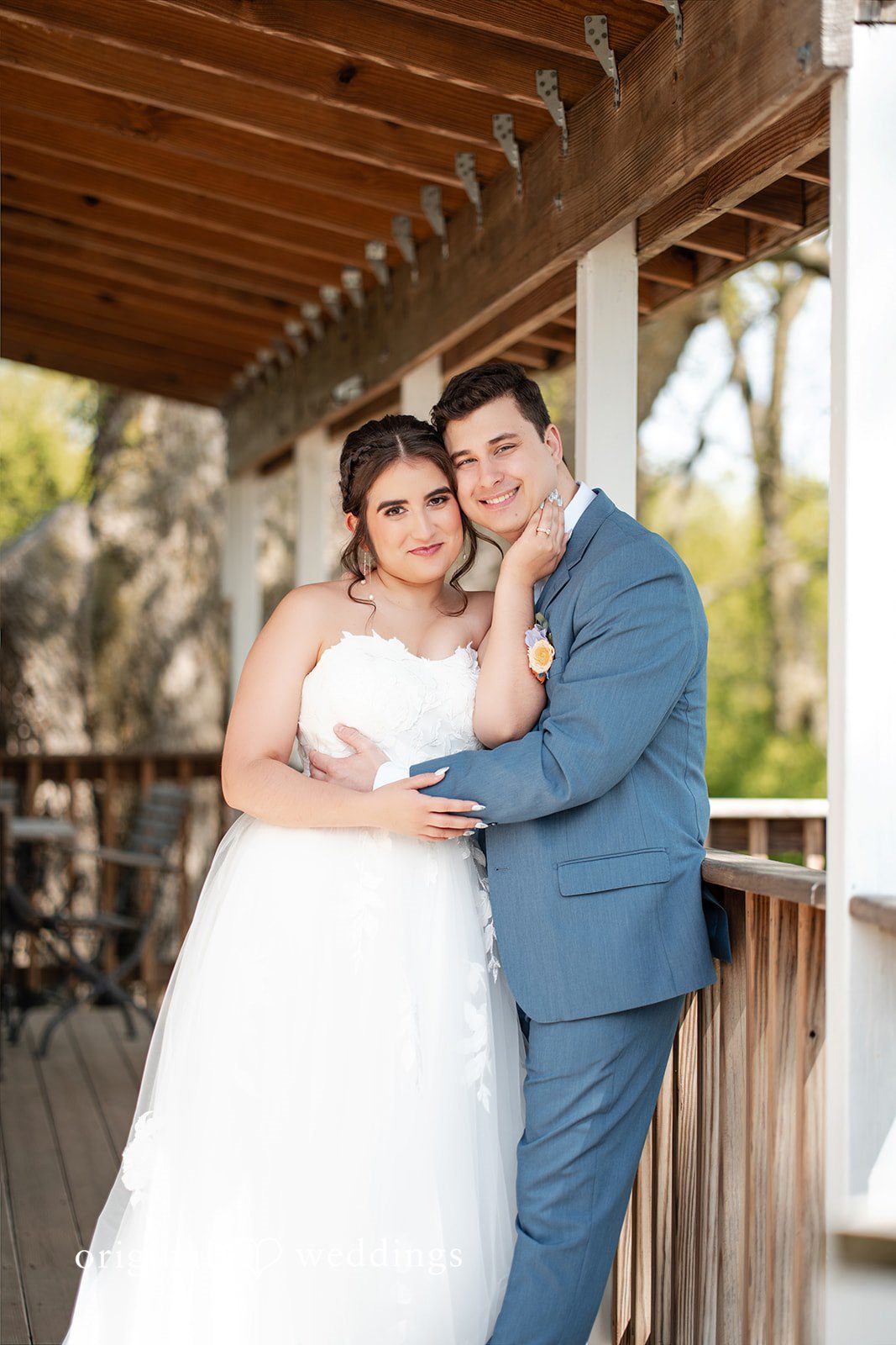 Bride and groom embracing on a rustic porch during their wedding portraits.