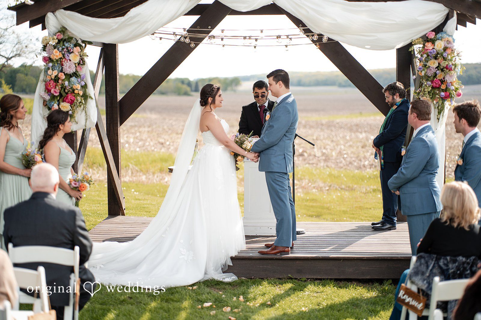 Outdoor wedding ceremony under a floral arch with the couple exchanging vows.