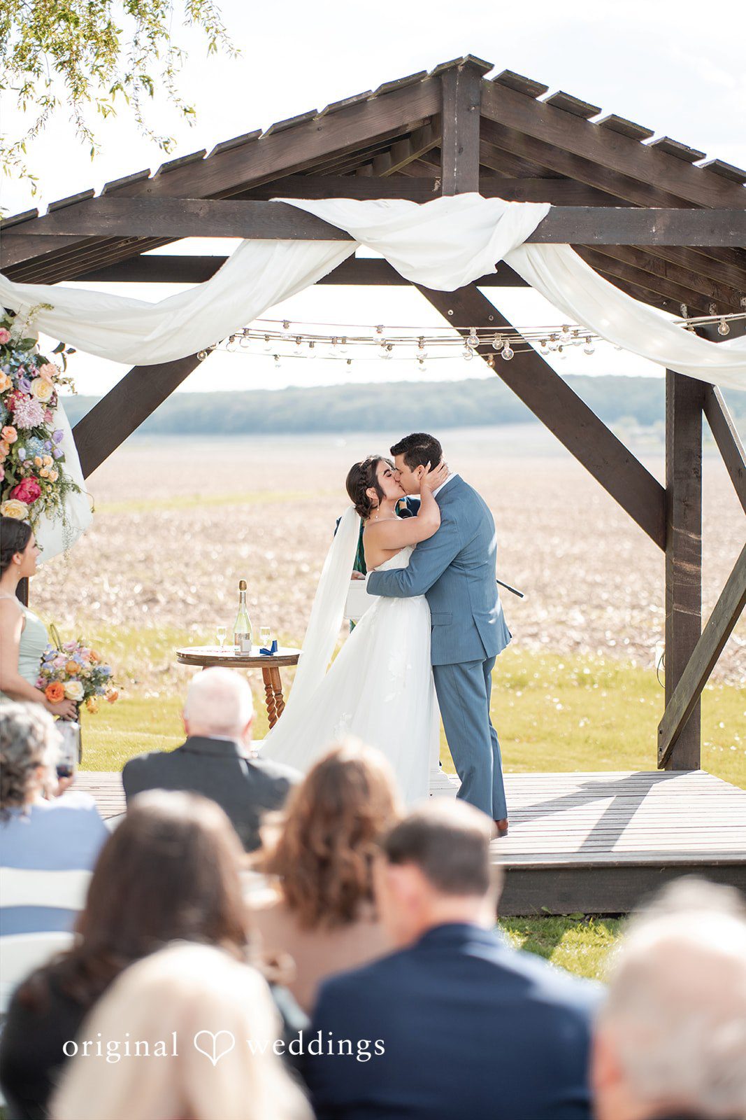 Bride and groom sharing their first kiss at an outdoor wedding ceremony.