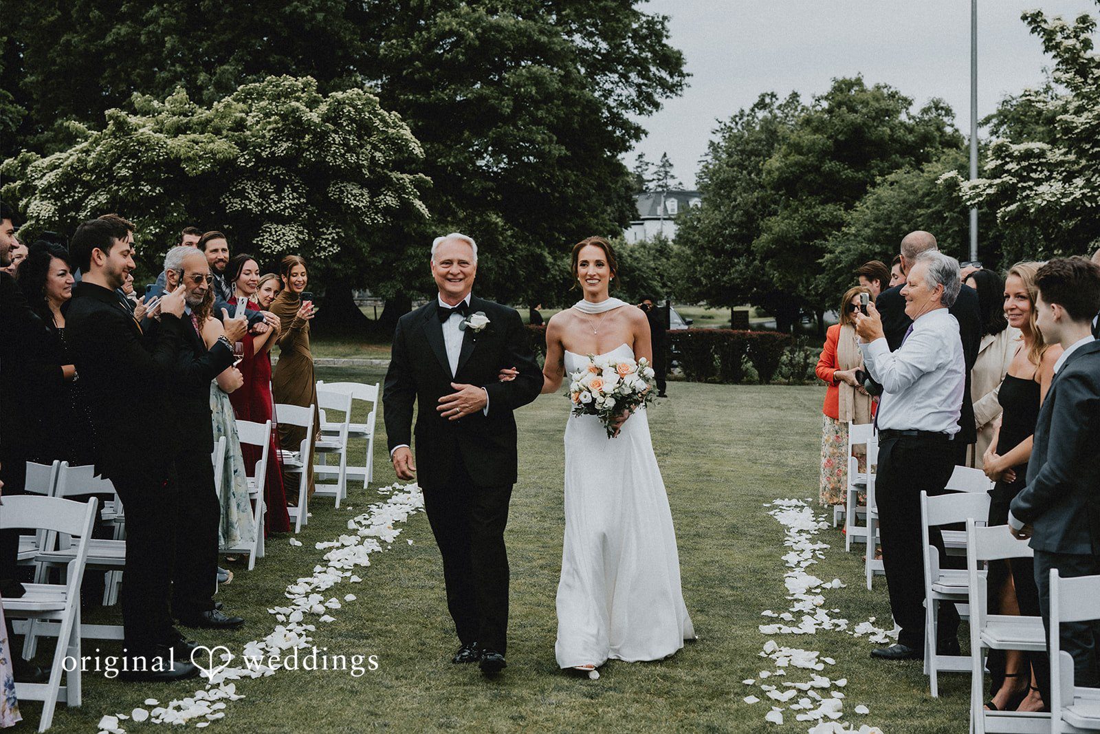 The bride and her father walk hand in hand down the aisle
