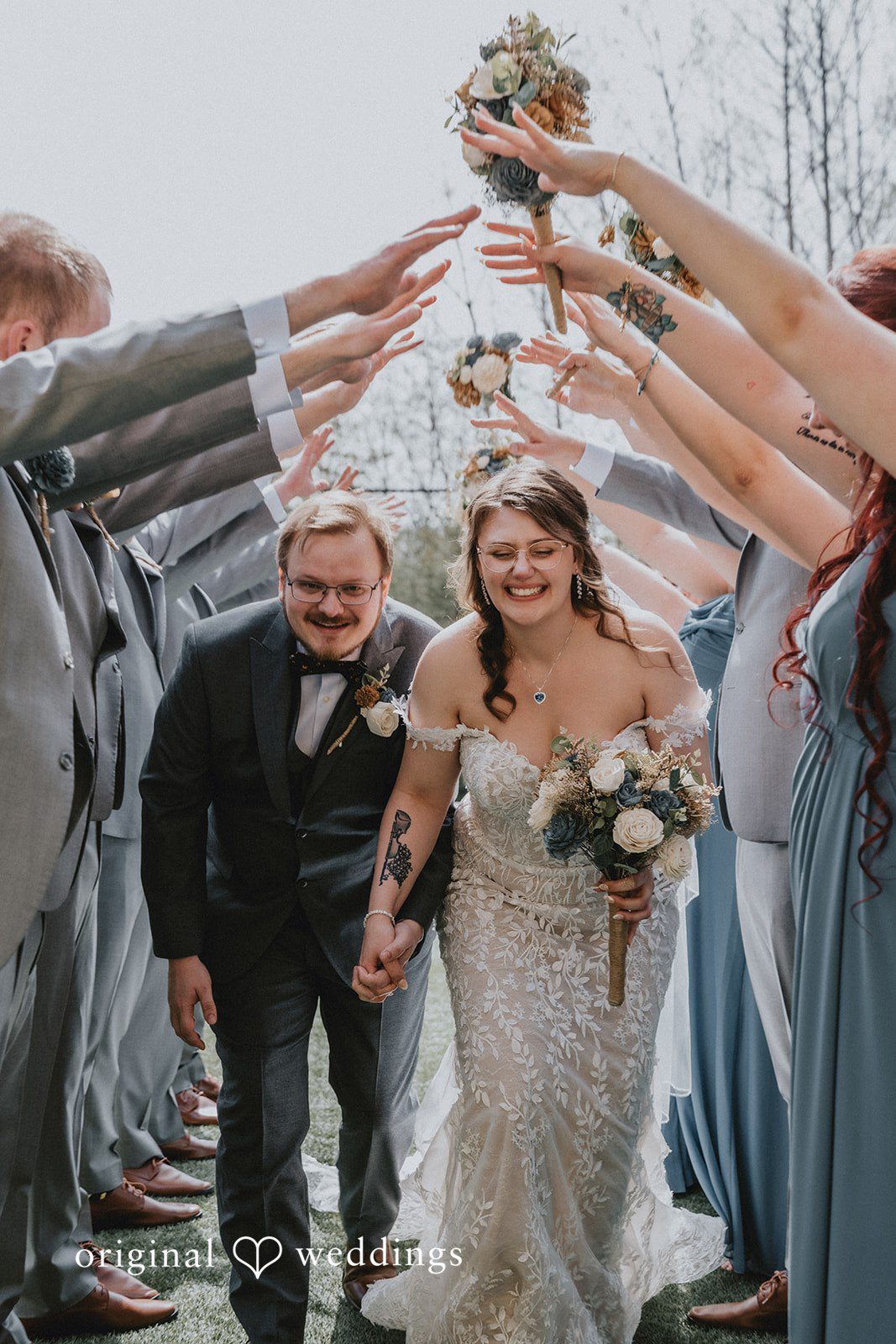 Ashlee + Colby Bride and groom walking beneath raised hands of their wedding party in a joyful moment