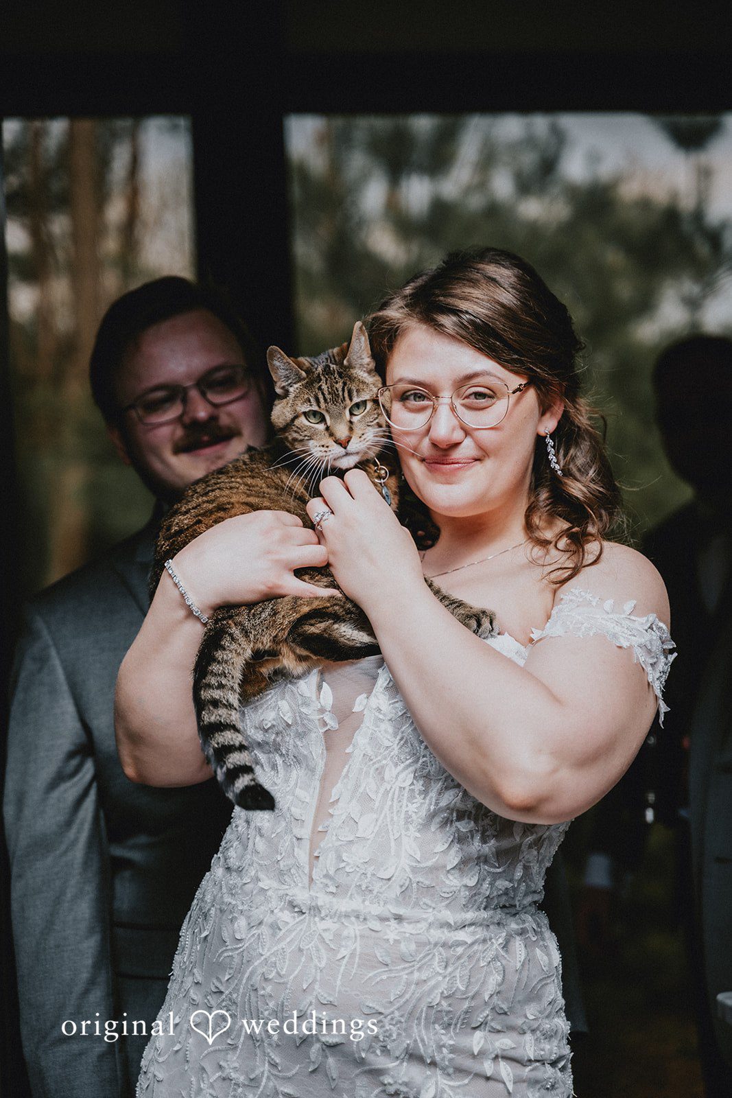 Ashlee + Colby Bride holding her cat while the groom stands behind her in a playful portrait