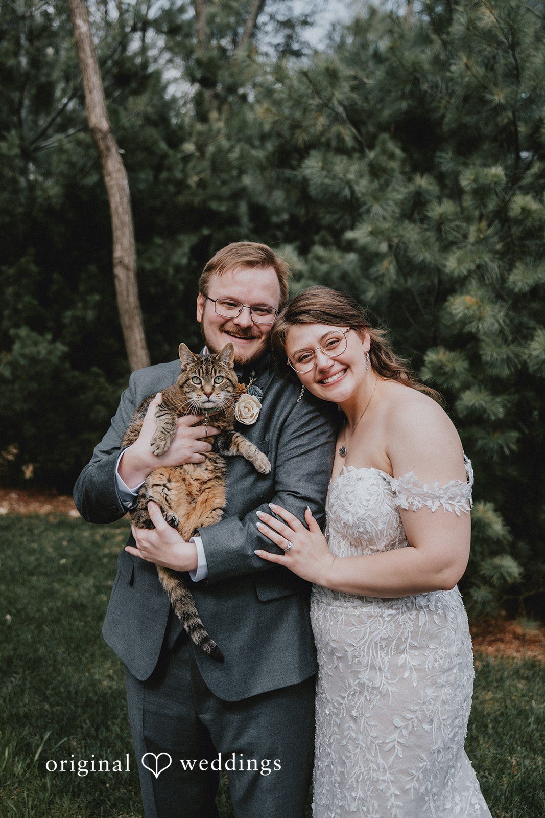 Ashlee + Colby Bride and groom posing with their cat among the trees in a full-length outdoor portrait