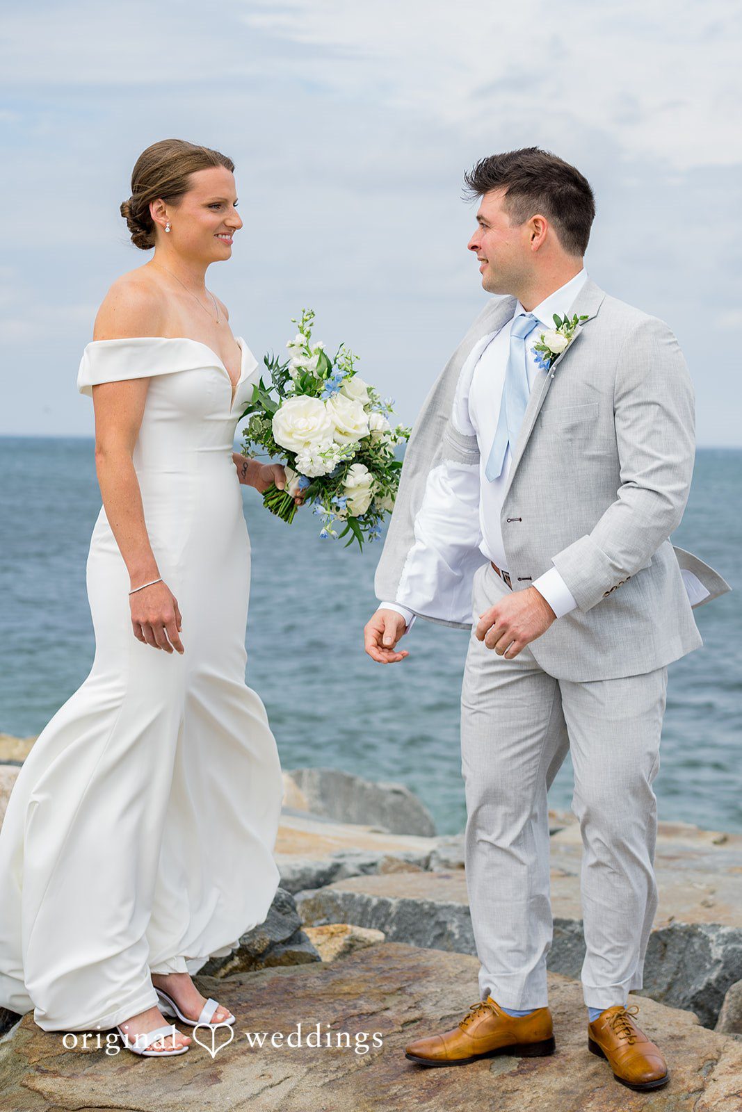 Molly + Joe A bride and groom face each other near a coastal landscape.
