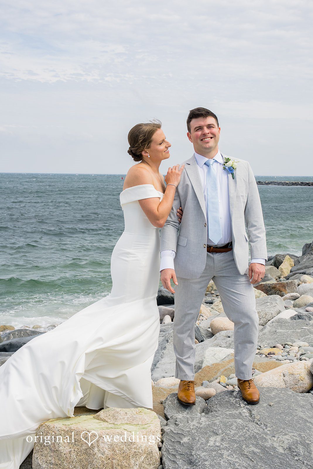 Molly + Joe A bride and groom smile and lean against each other on a rocky shoreline.