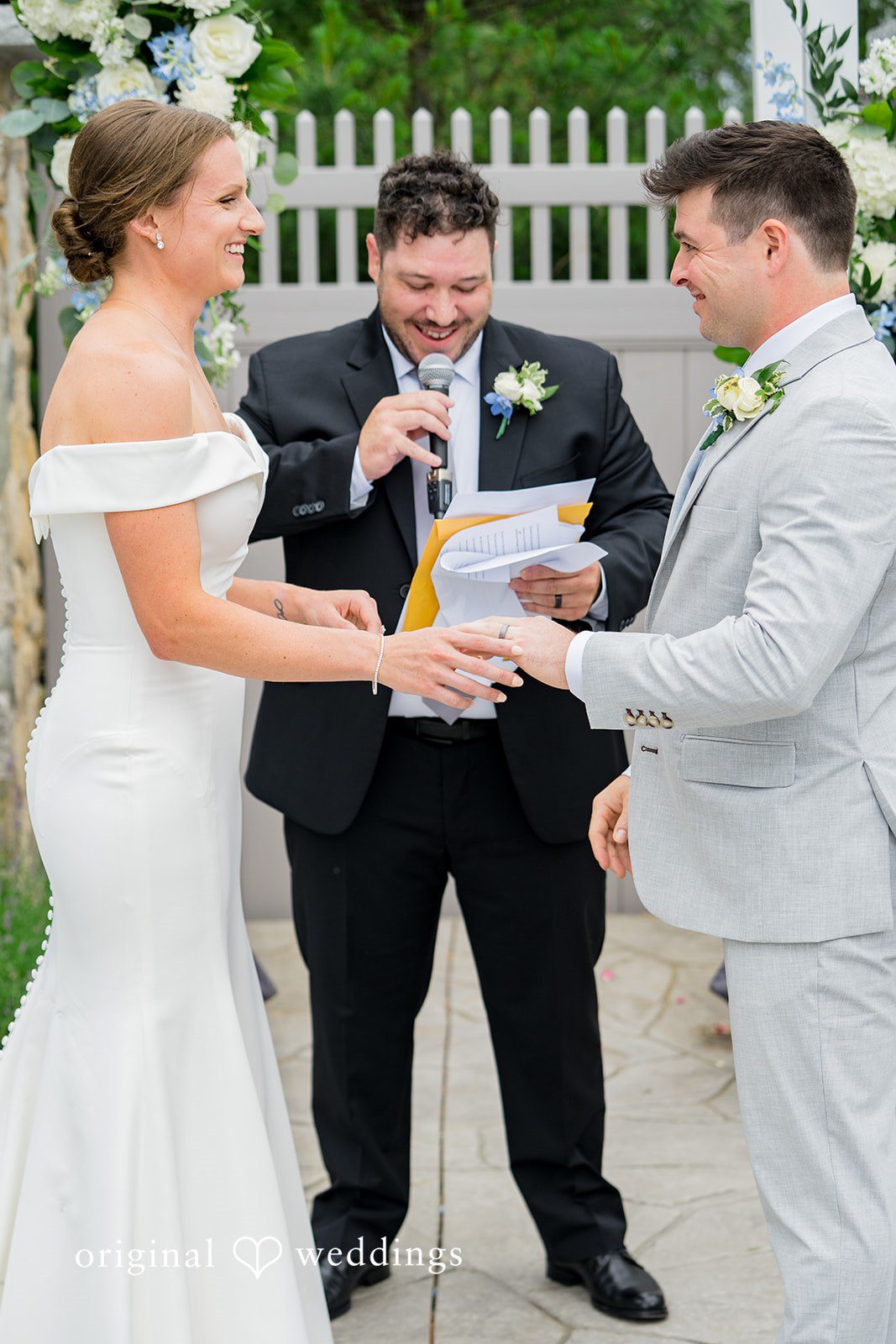 Molly + Joe A bride and groom exchange rings during their wedding ceremony in front of an officiant.
