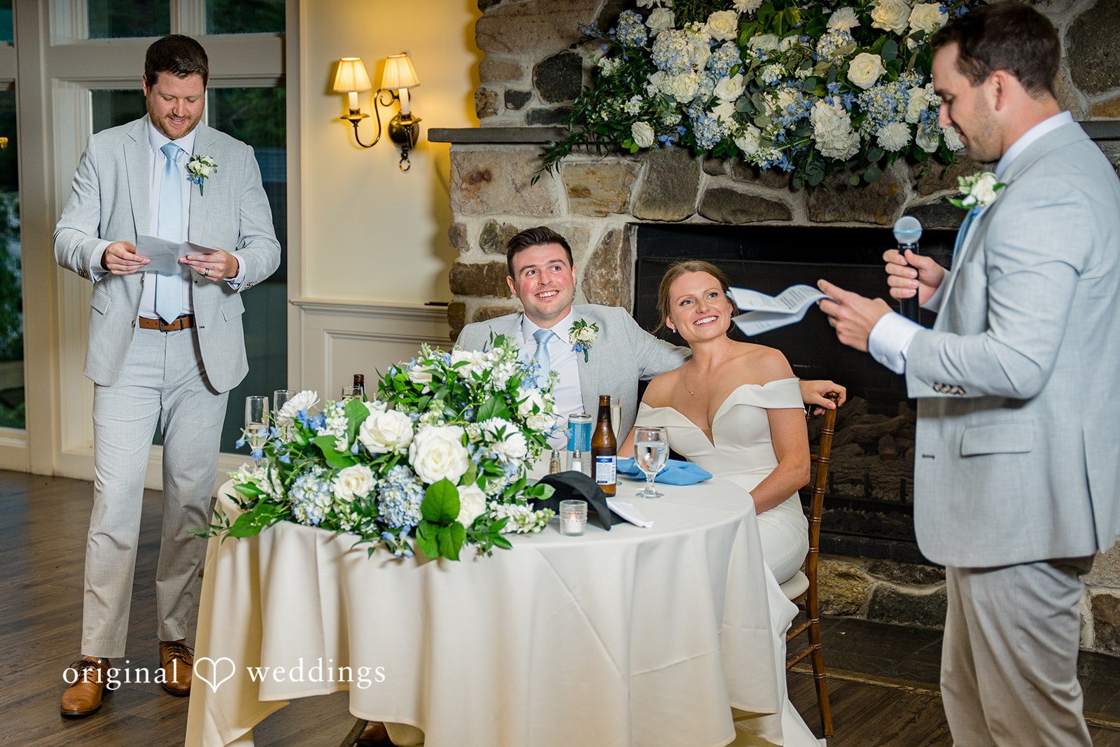 Molly + Joe A bride and groom sit at their reception table while a guest delivers a speech.