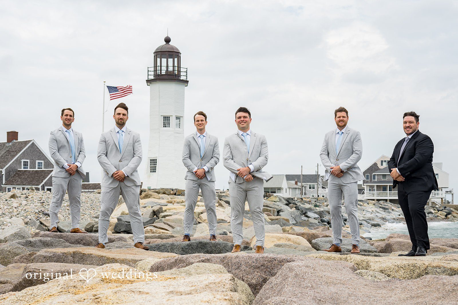 Molly + Joe A groom and groomsmen in matching light gray suits stand posing near a lighthouse.