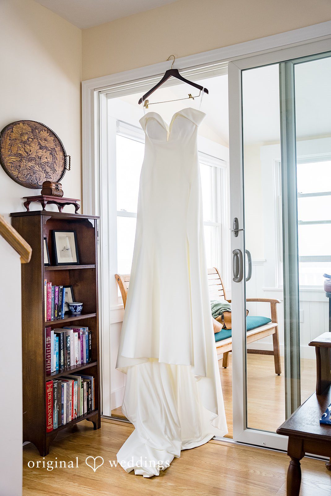 Molly + Joe A white wedding gown hangs from a hanger in a brightly lit room.