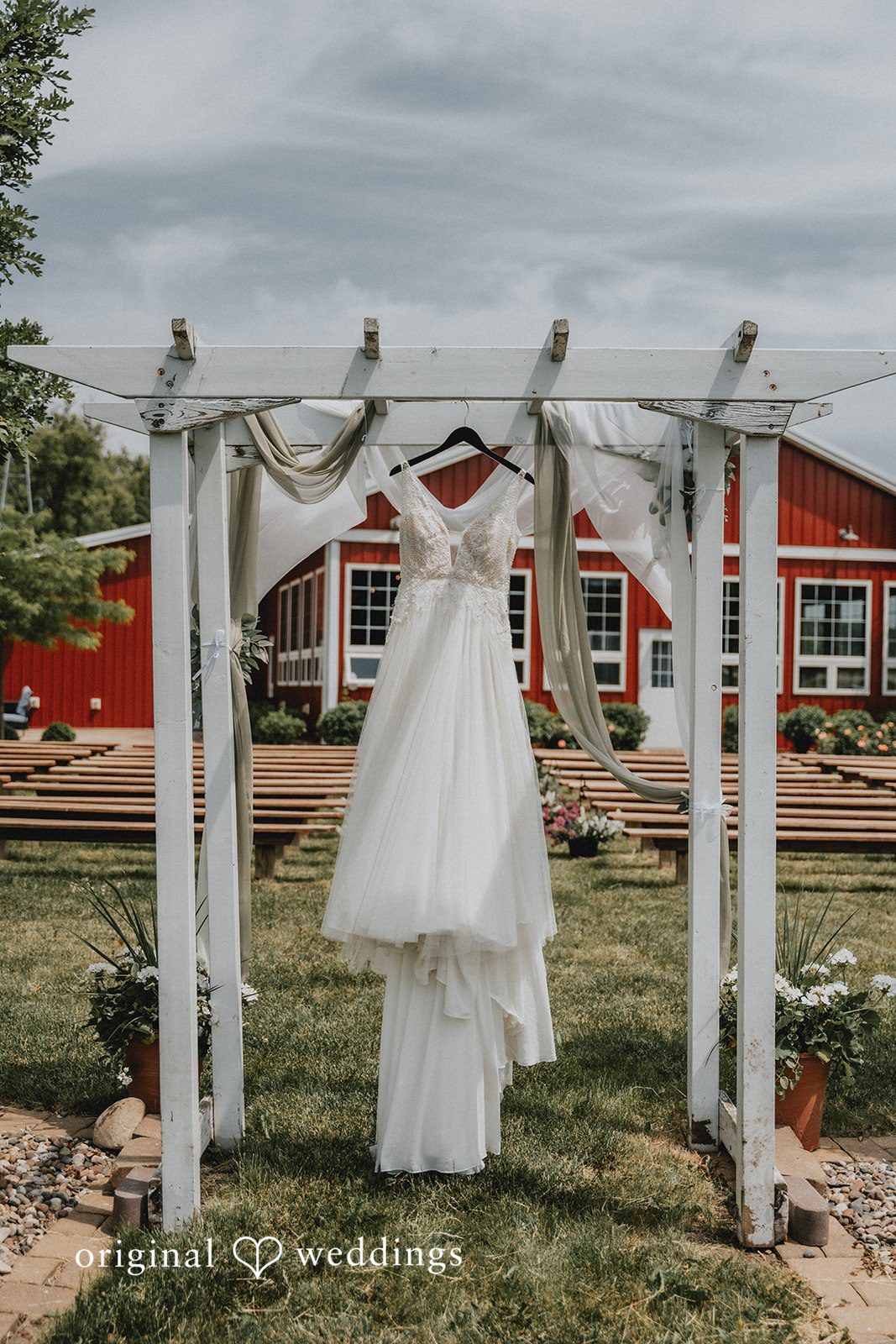Neil + Hallie A white wedding dress hanging inside an open-air wooden arch structure.