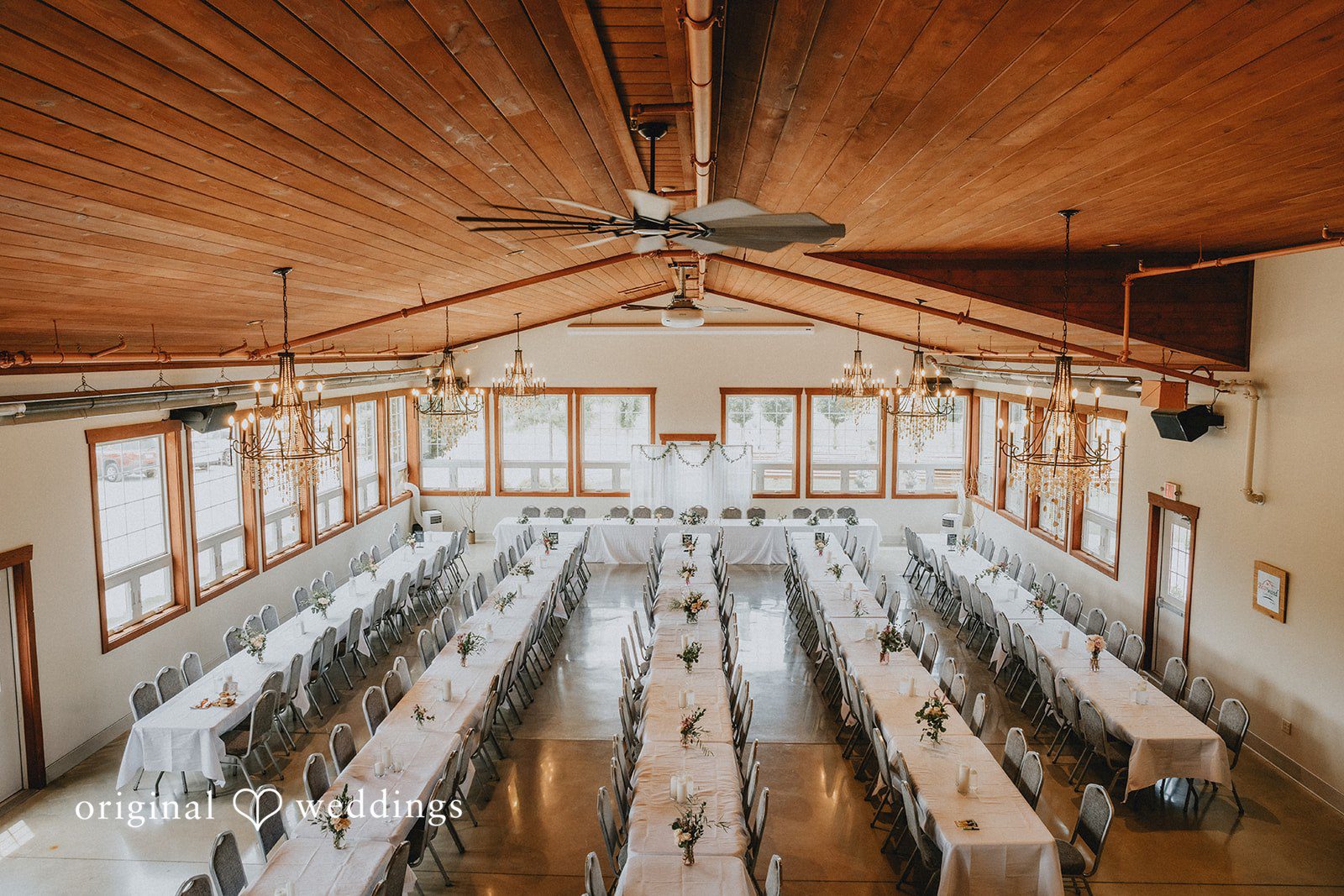 Neil + Hallie High-angle view of a large wedding reception hall filled with long wooden tables.