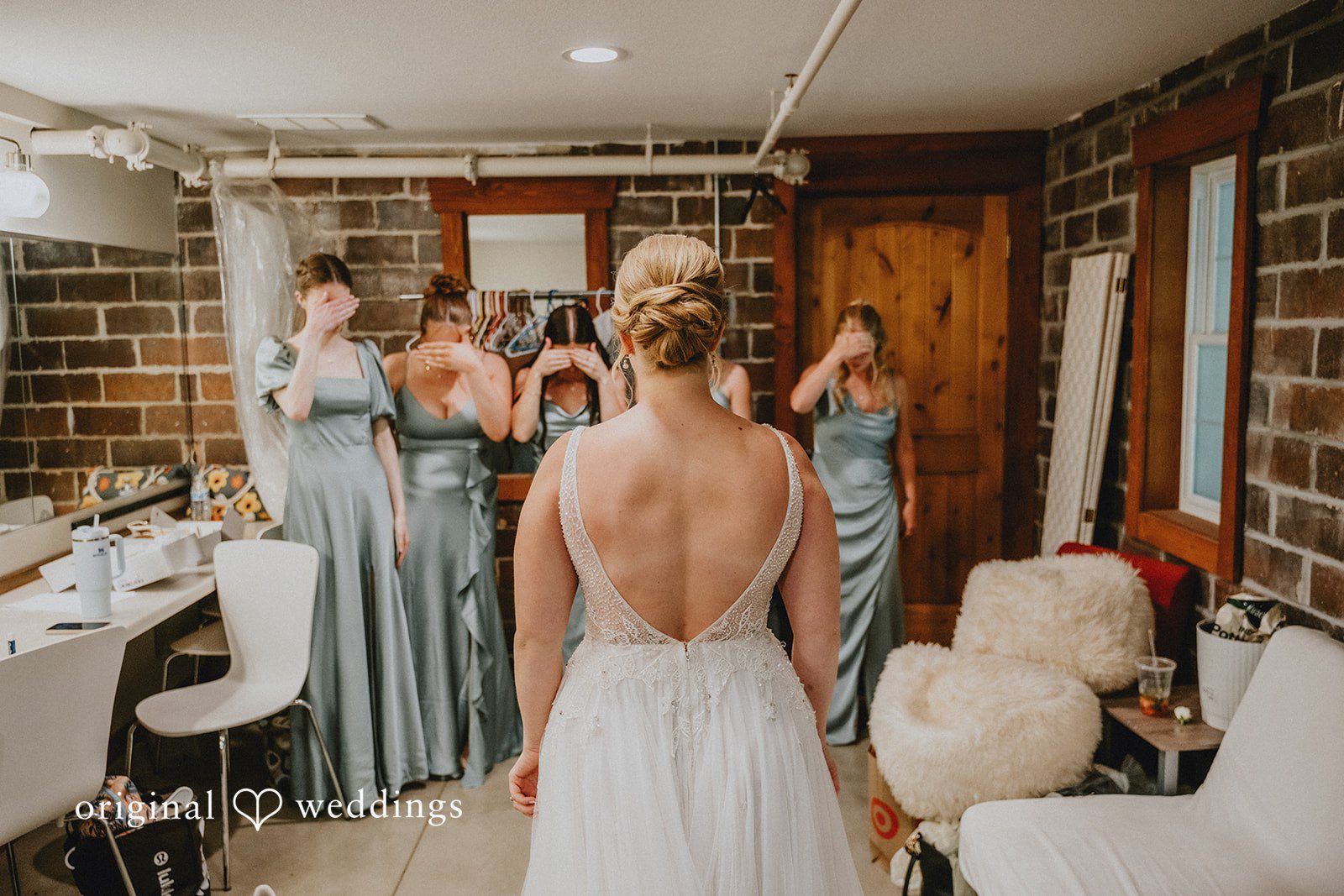 Neil + Hallie Back view of a bride standing in a room with her bridesmaids.