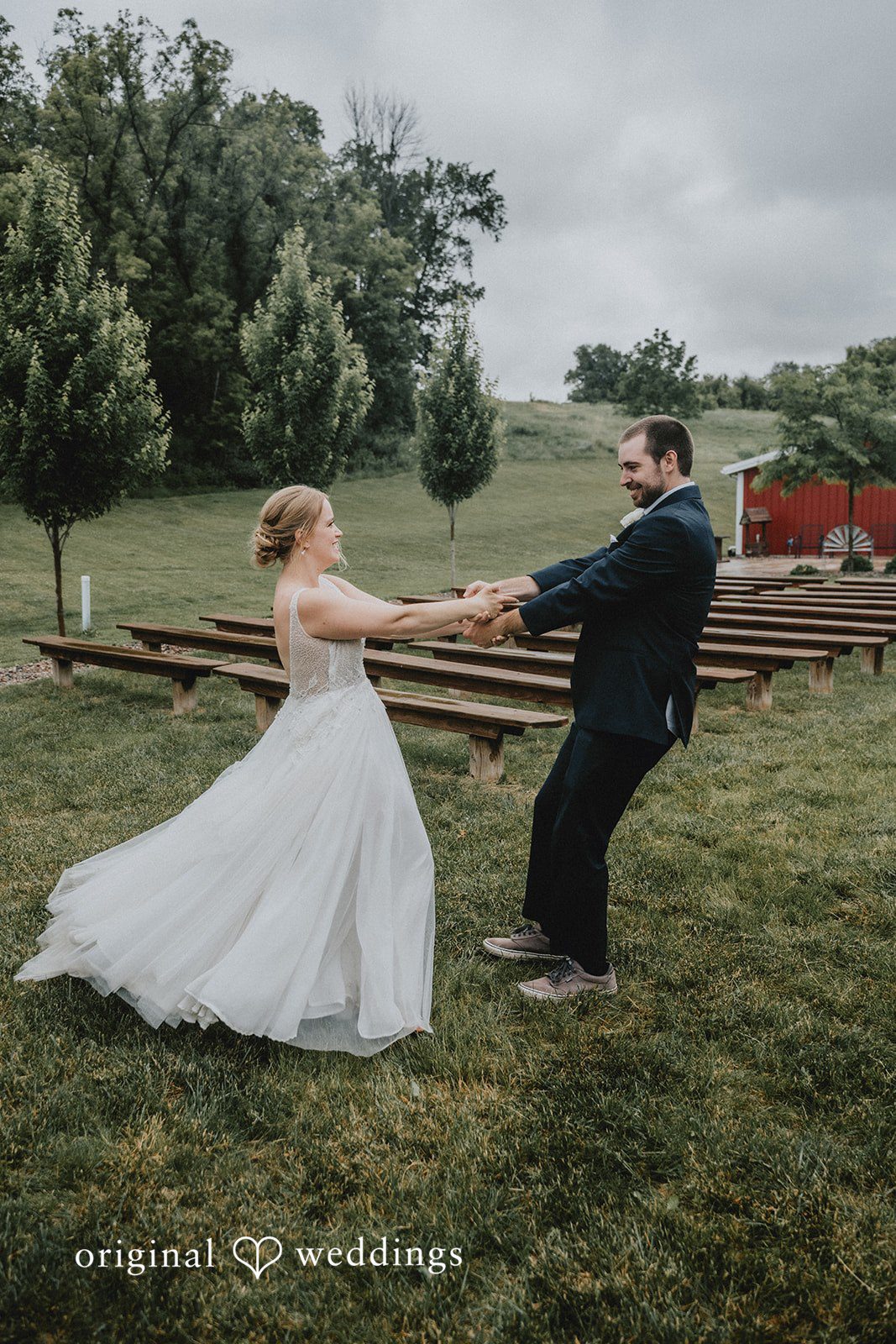 Neil + Hallie A bride and groom holding hands and joyfully spinning together on a field.