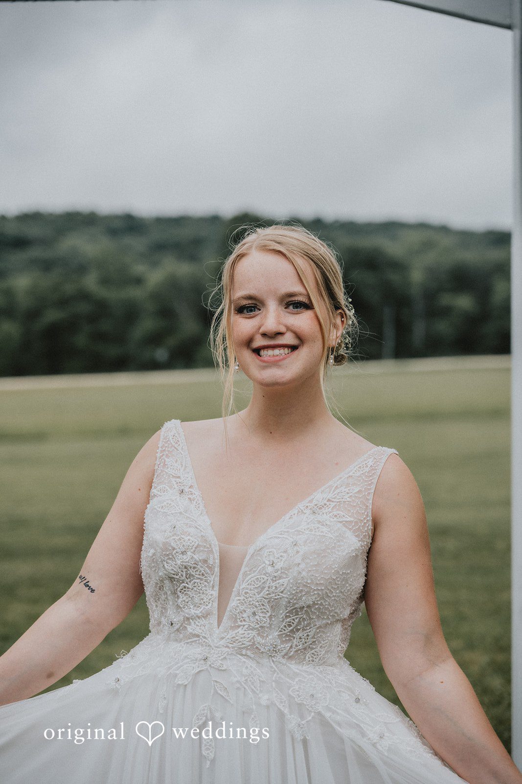 Neil + Hallie A smiling blonde bride posing in her white wedding gown on a field.