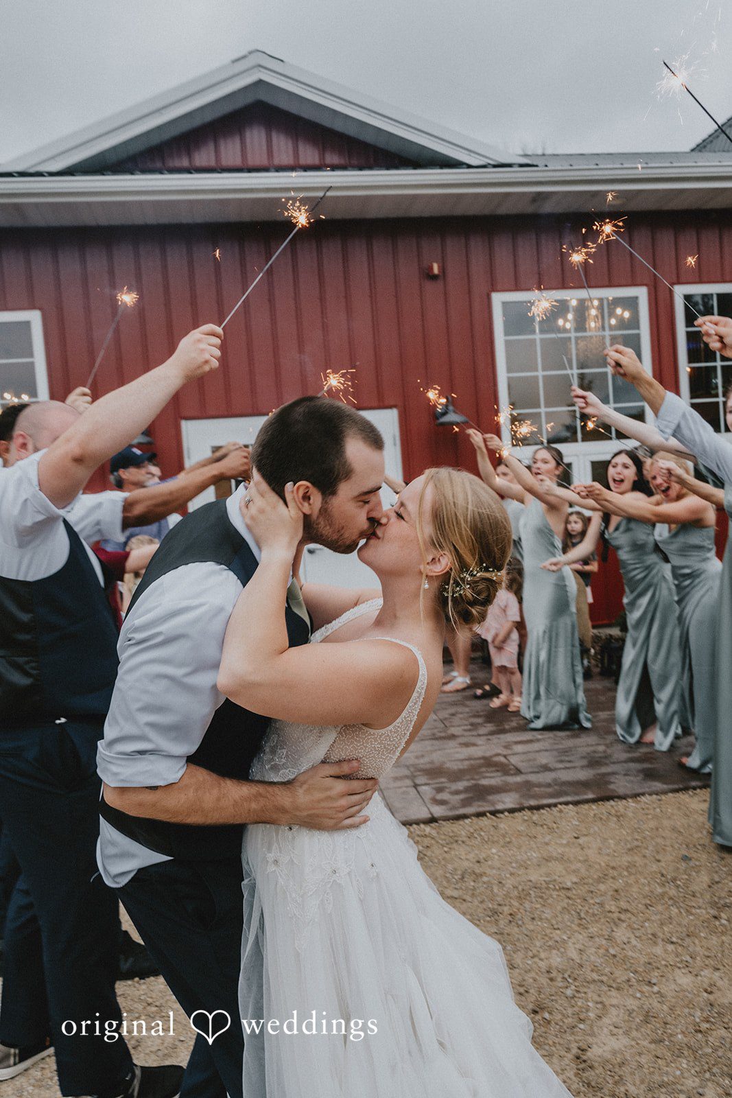 Neil + Hallie A bride and groom sharing a kiss while wedding guests celebrate around them.
