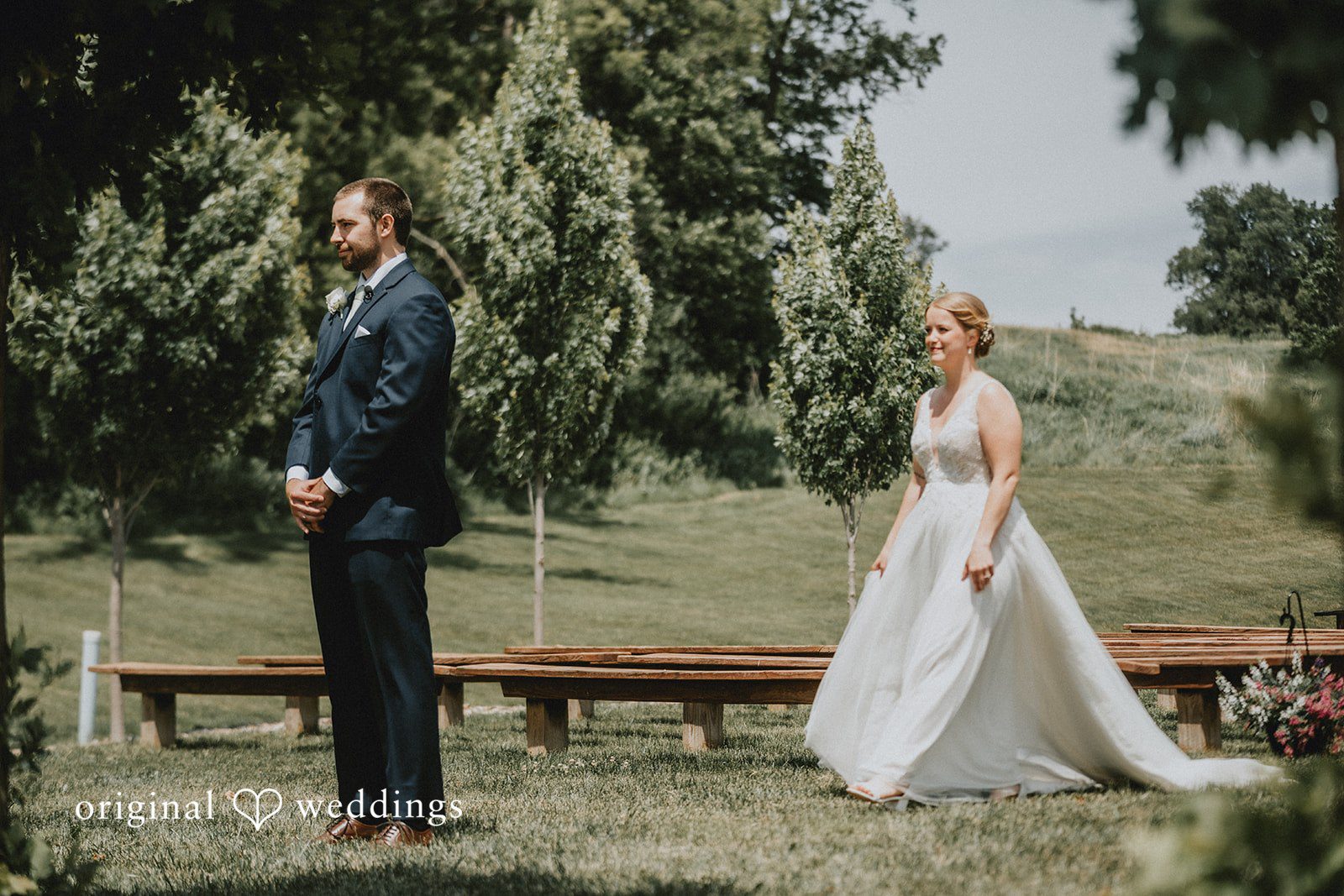 Neil + Hallie A bride and groom standing apart on a grassy field, looking toward each other.