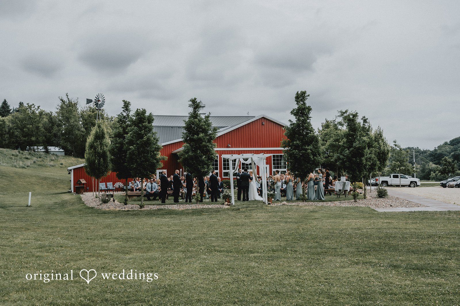 Neil + Hallie A wide shot of a wedding venue with a red building and green grass.