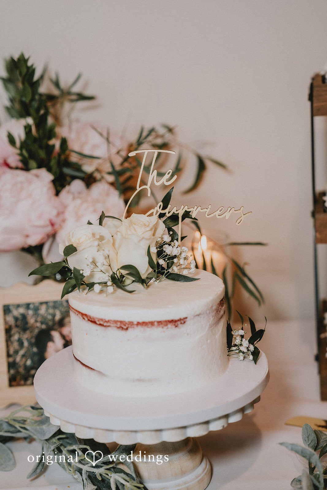 Neil + Hallie A multi-tiered white wedding cake topped with flowers on a rustic stand.