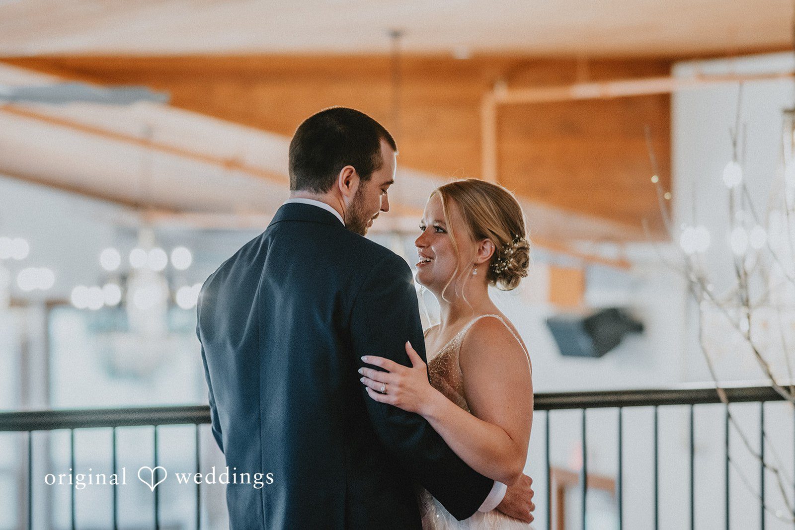 Neil + Hallie A groom hugging his bride from behind on an elevated balcony or deck.
