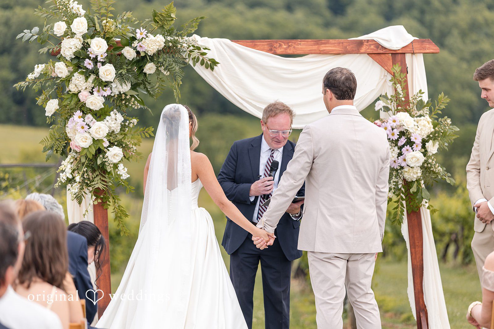 Brett + Ava Couple listening to the priest holding hands during wedding ceremony at Breaux Vineyards