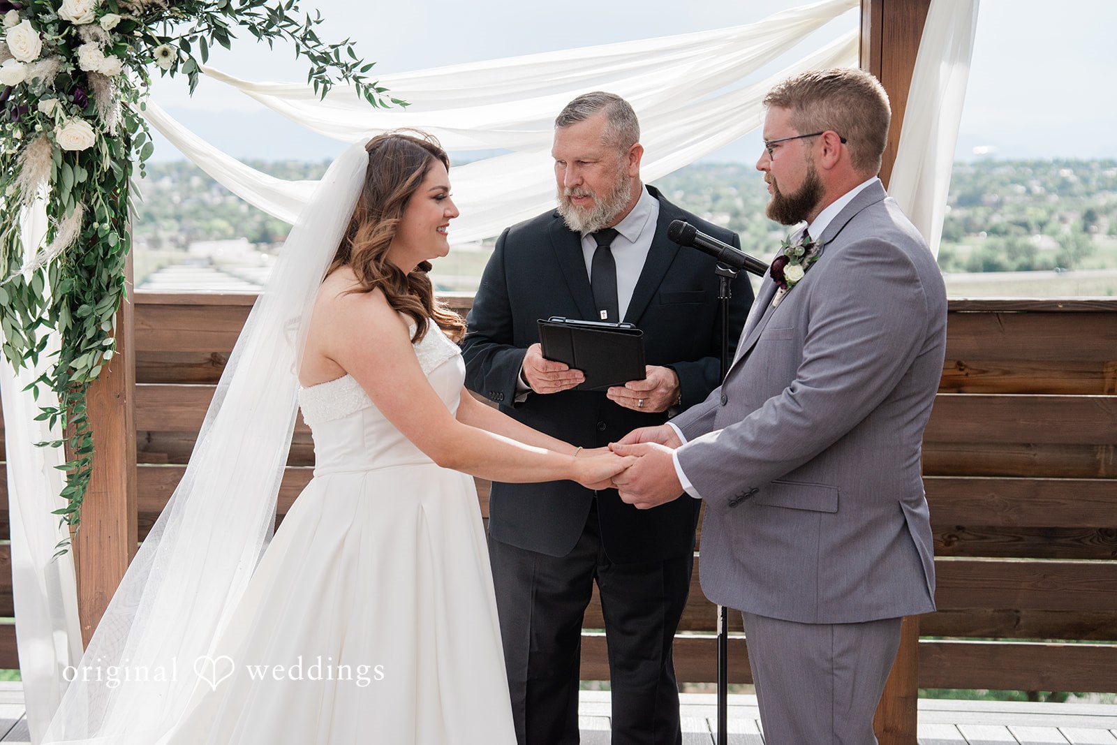 Carolina + Jonah Couple standing before the priest during the ceremony while holding hands at Brittany Hill - Wedgewood Weddings