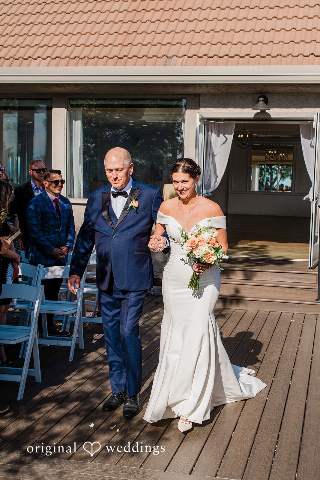Rachel & Krystal A bride and man in formal attire walking down an aisle together.