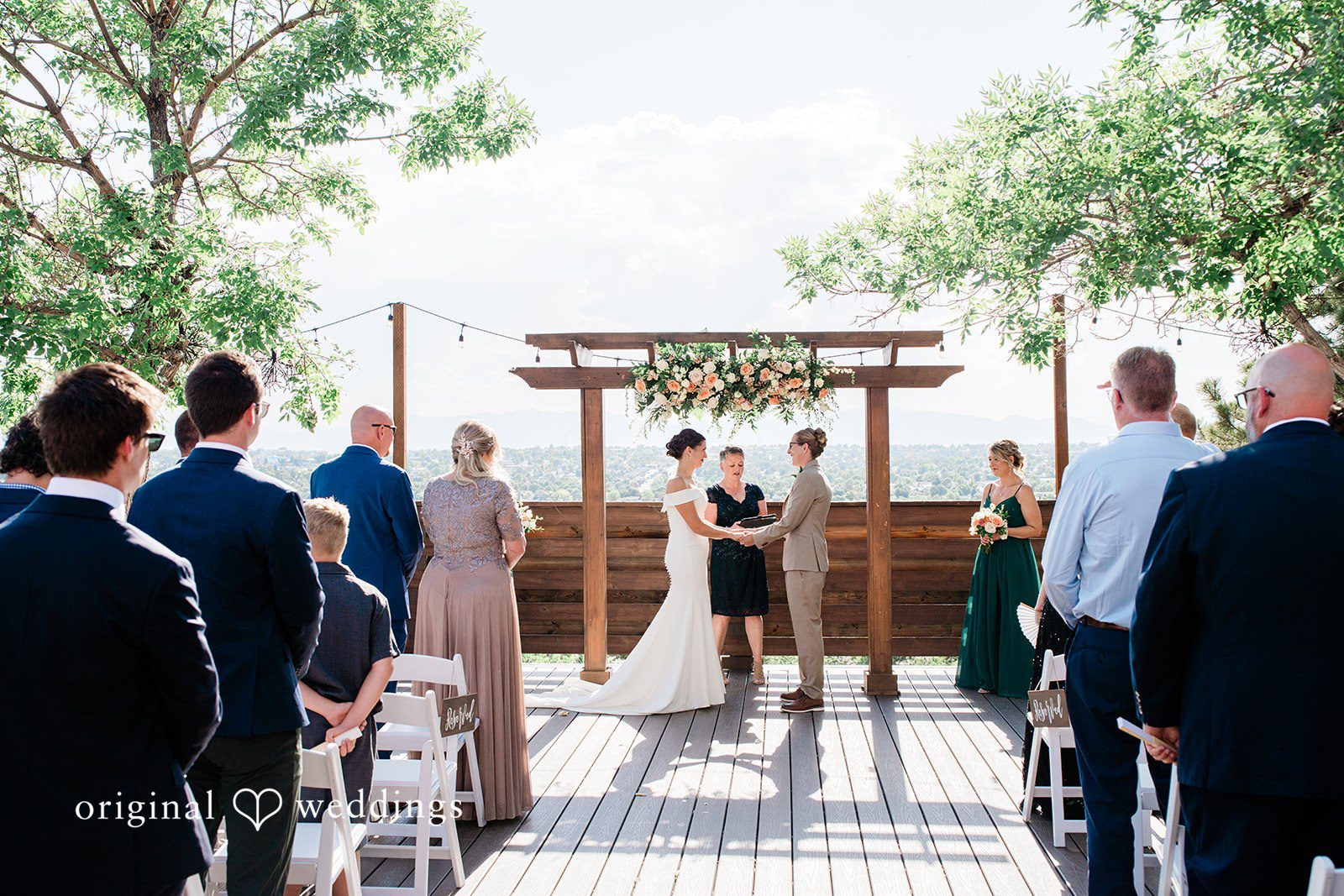 Rachel & Krystal Guests seated in rows watching a wedding ceremony under a wooden arbor.