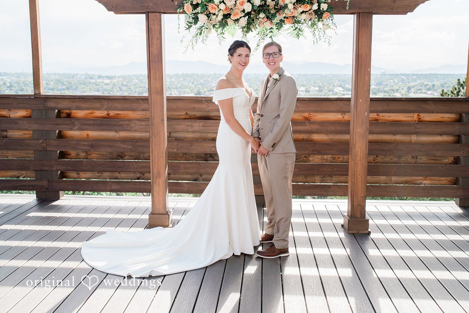 Rachel & Krystal A wedding couple posing together under a wooden pergola structure.