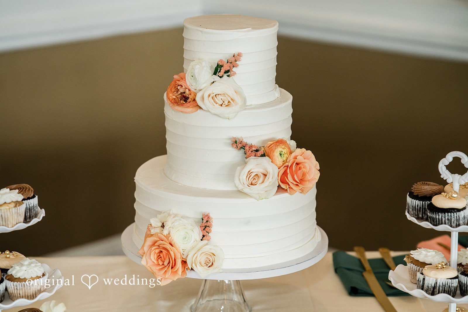 Rachel & Krystal A three-tiered white wedding cake decorated with orange and pink flowers.
