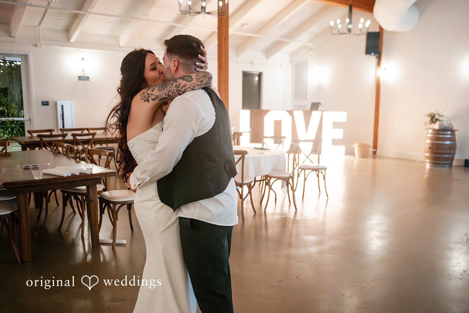 Noah + Jade A bride and groom sharing an intimate embrace on the dance floor with a lit-up "LOVE" sign in the background.