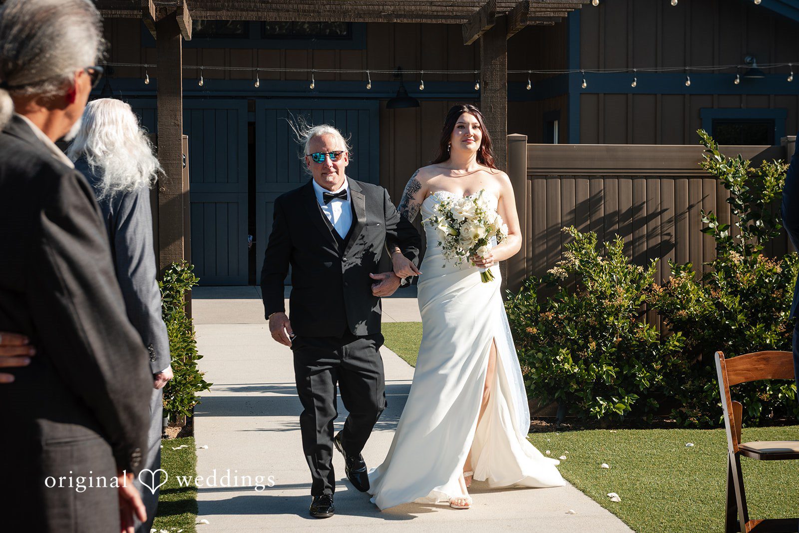 Noah + Jade A bride walking down an aisle arm-in-arm with an older man in a tuxedo.