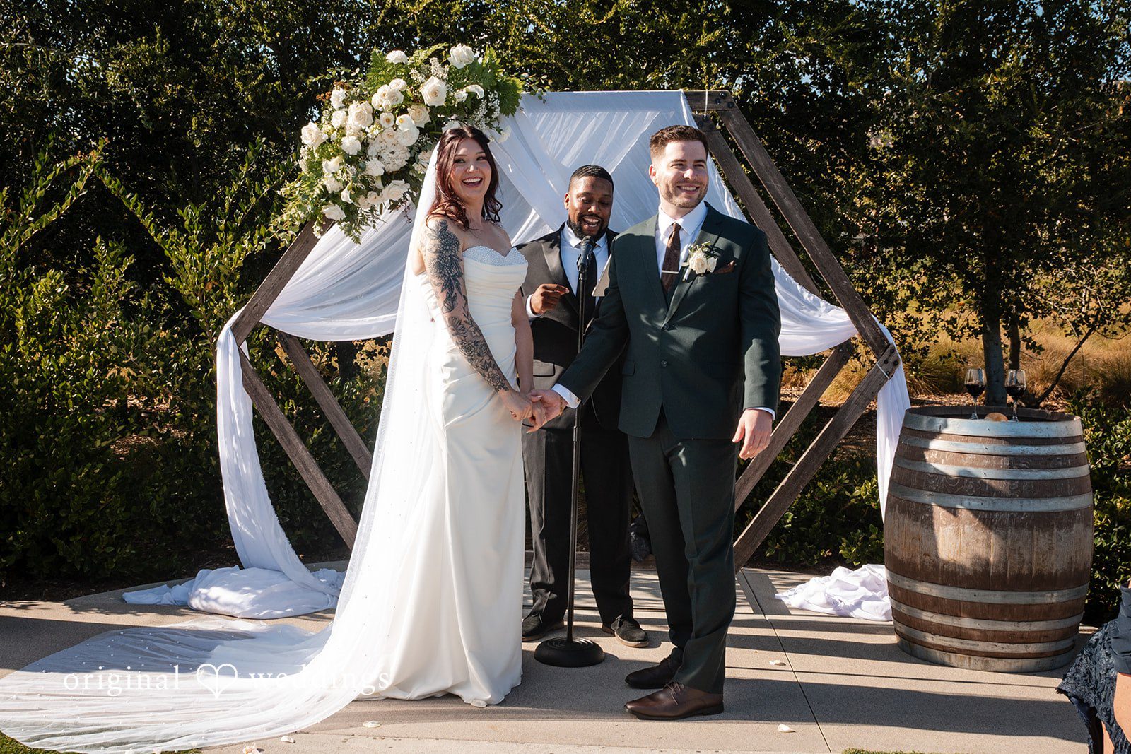 Noah + Jade A bride and groom standing together at a wooden geometric wedding arch during their ceremony.