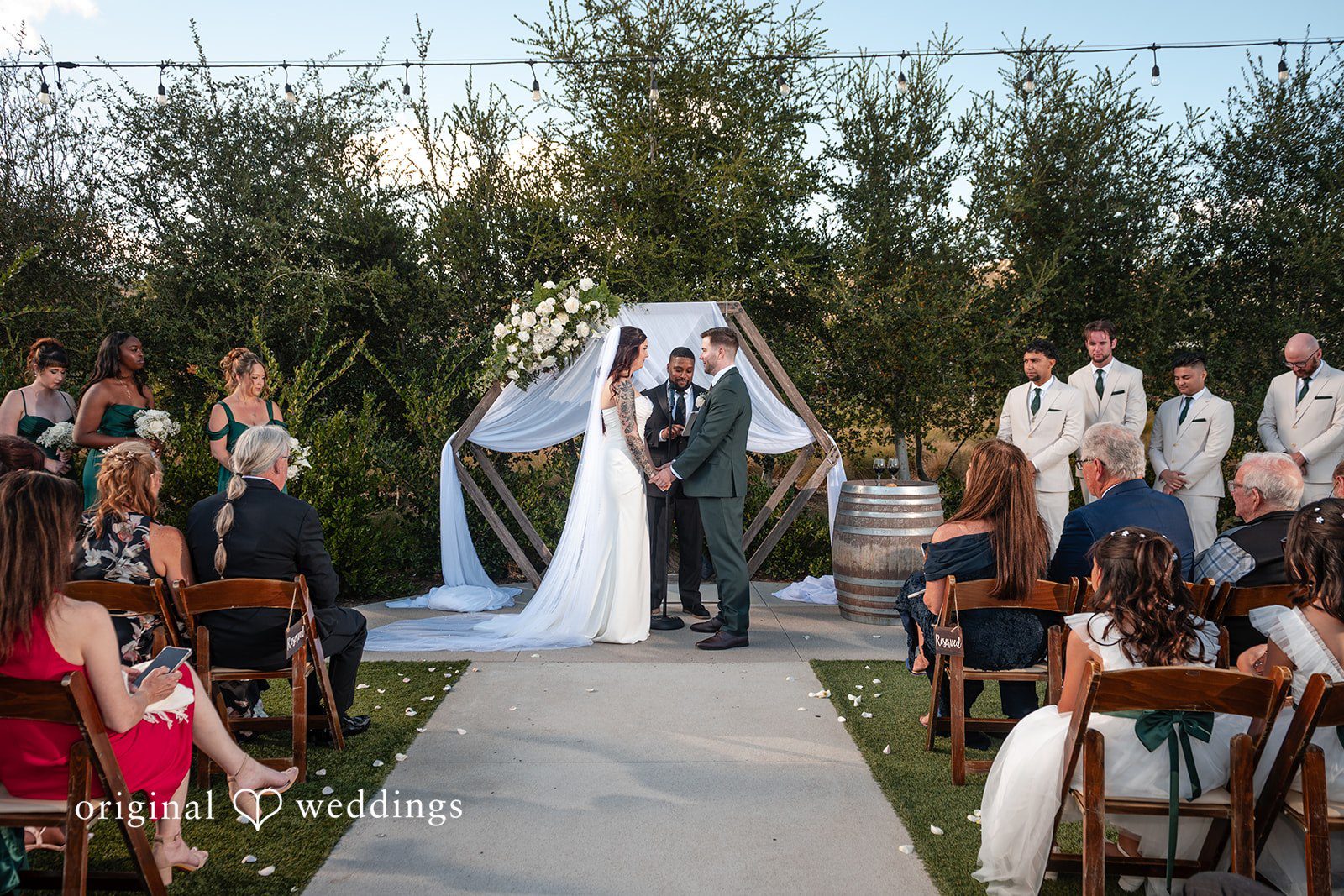Noah + Jade A wide view of a wedding ceremony in progress with guests seated in wooden chairs.
