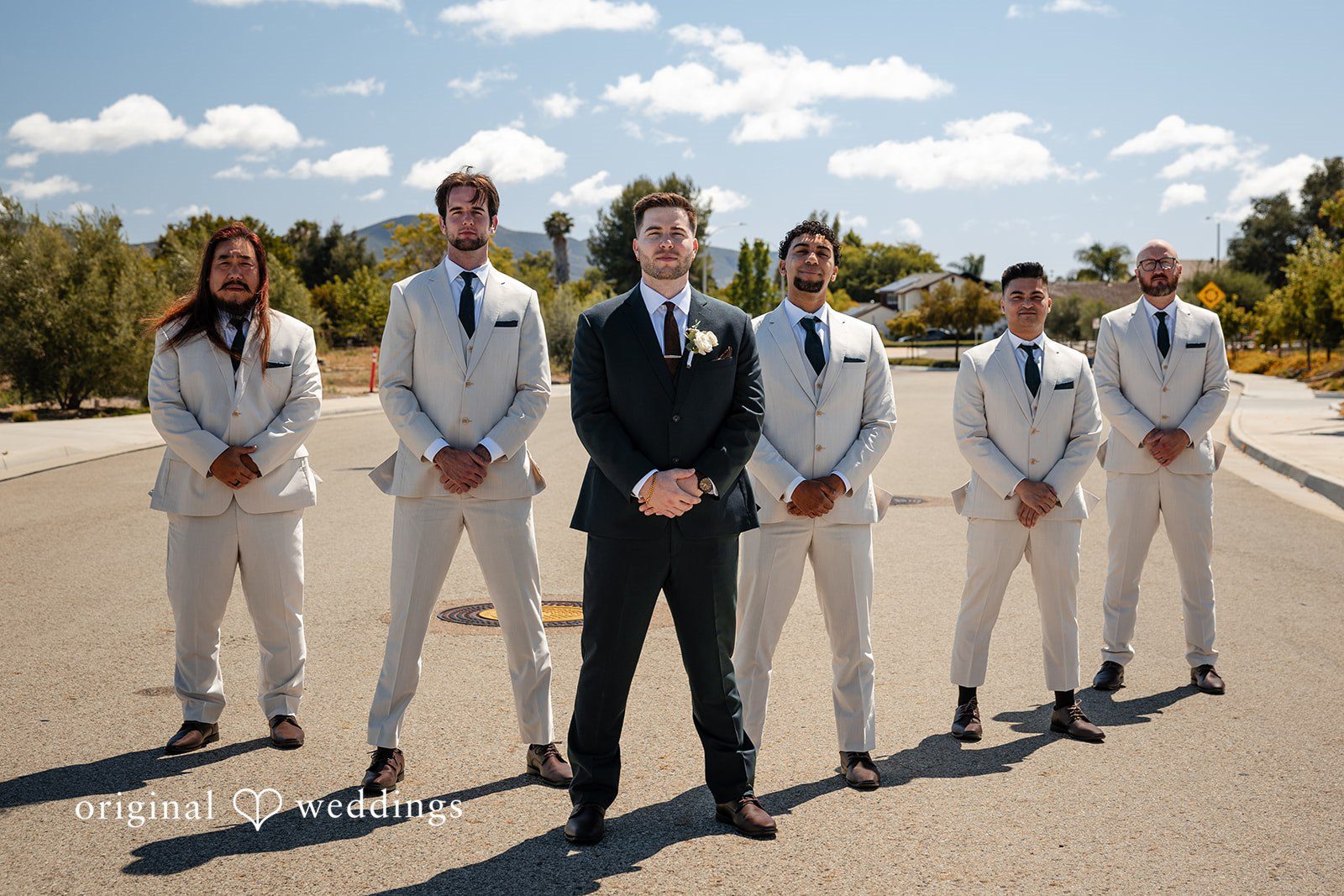 Noah + Jade A groom in a black suit standing forward with groomsmen in light-colored suits behind him.