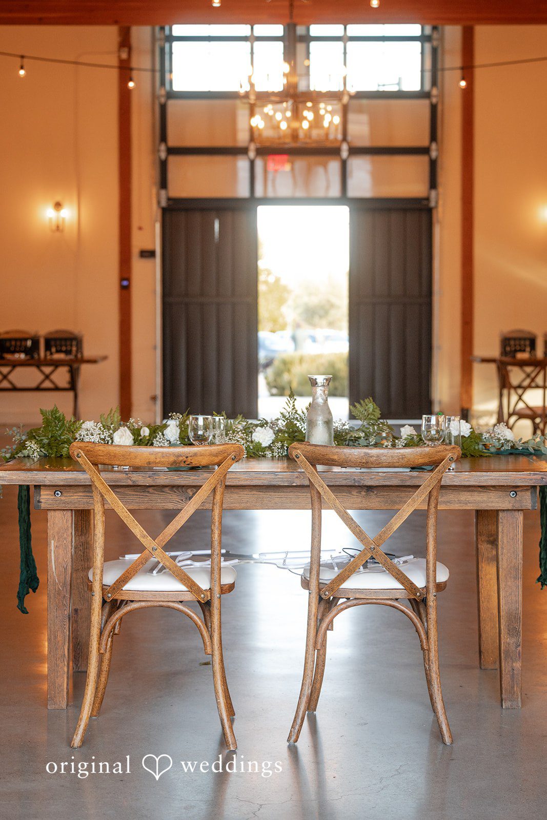 Noah + Jade Set wedding reception table with cross-back wooden chairs, plates, glassware, and floral centerpieces.