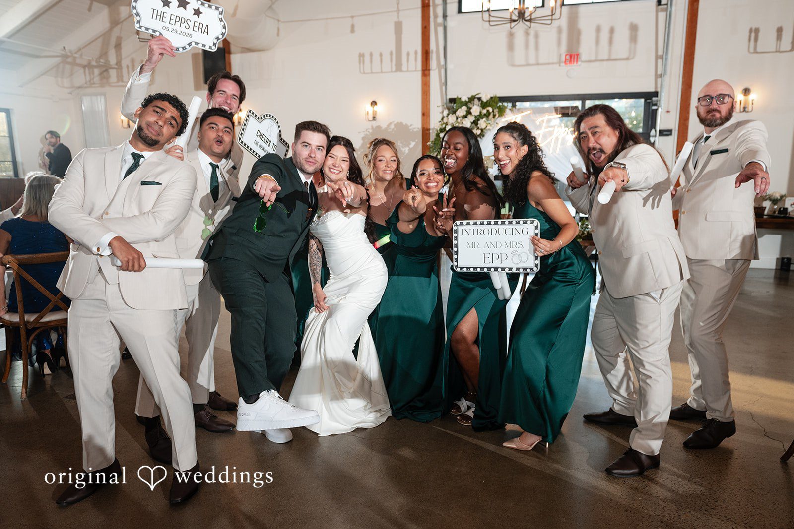 Noah + Jade A large, enthusiastic wedding party posing together for a fun group photo while holding signs.