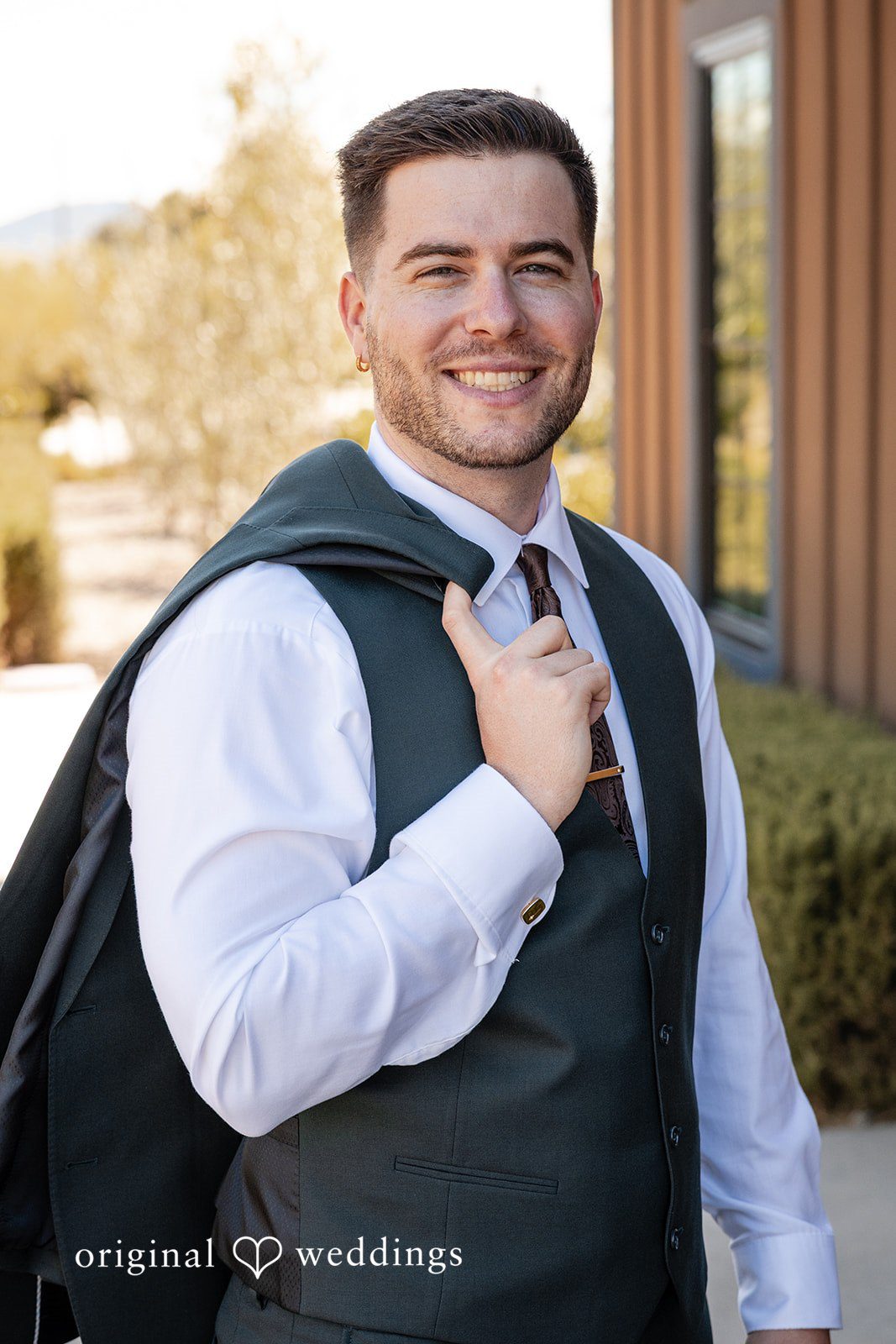 Noah + Jade A smiling groom in a dark vest slinging his jacket over his shoulder.