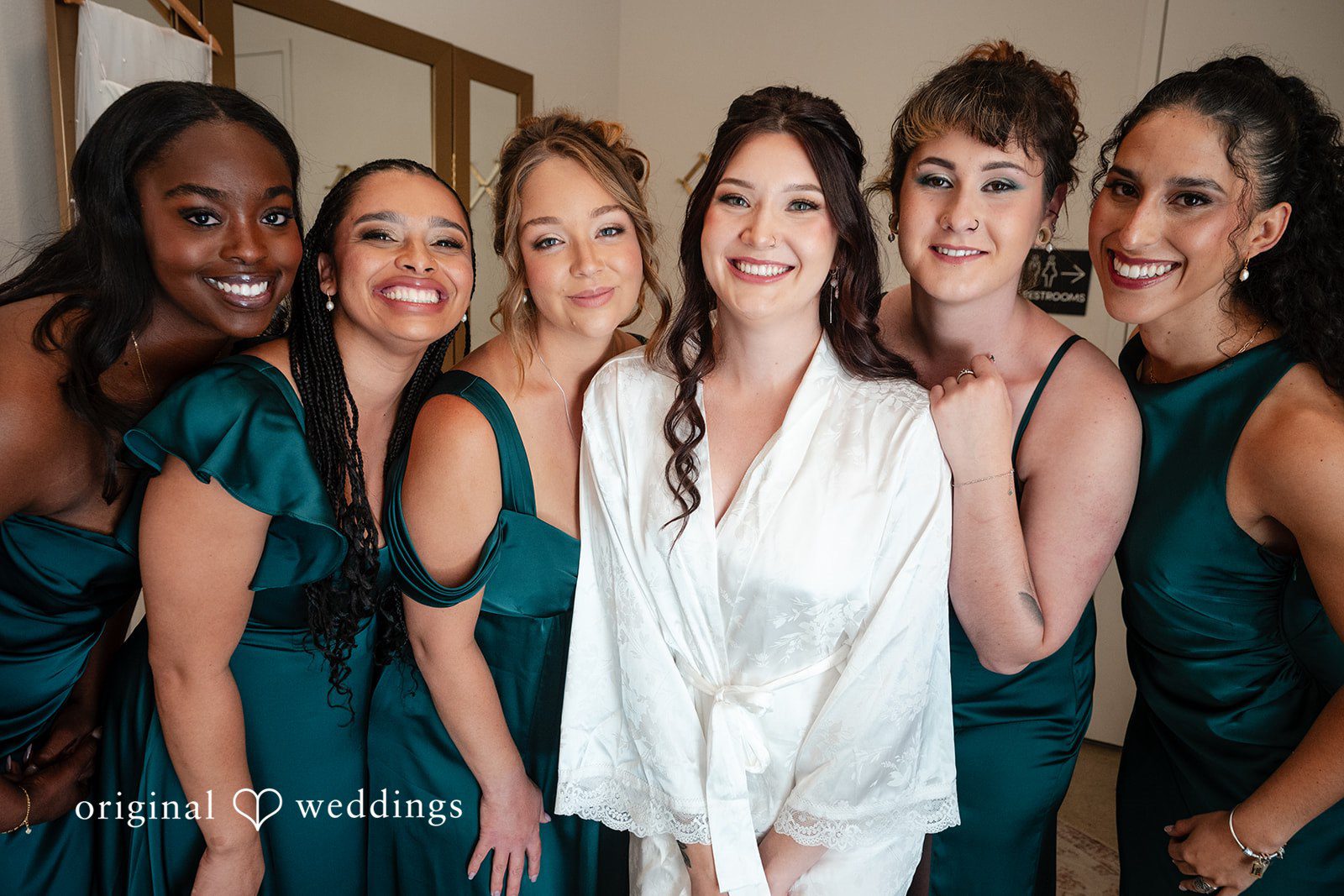 Noah + Jade Bride wearing a white silk robe standing in the center of her bridesmaids who are dressed in matching deep green gowns.